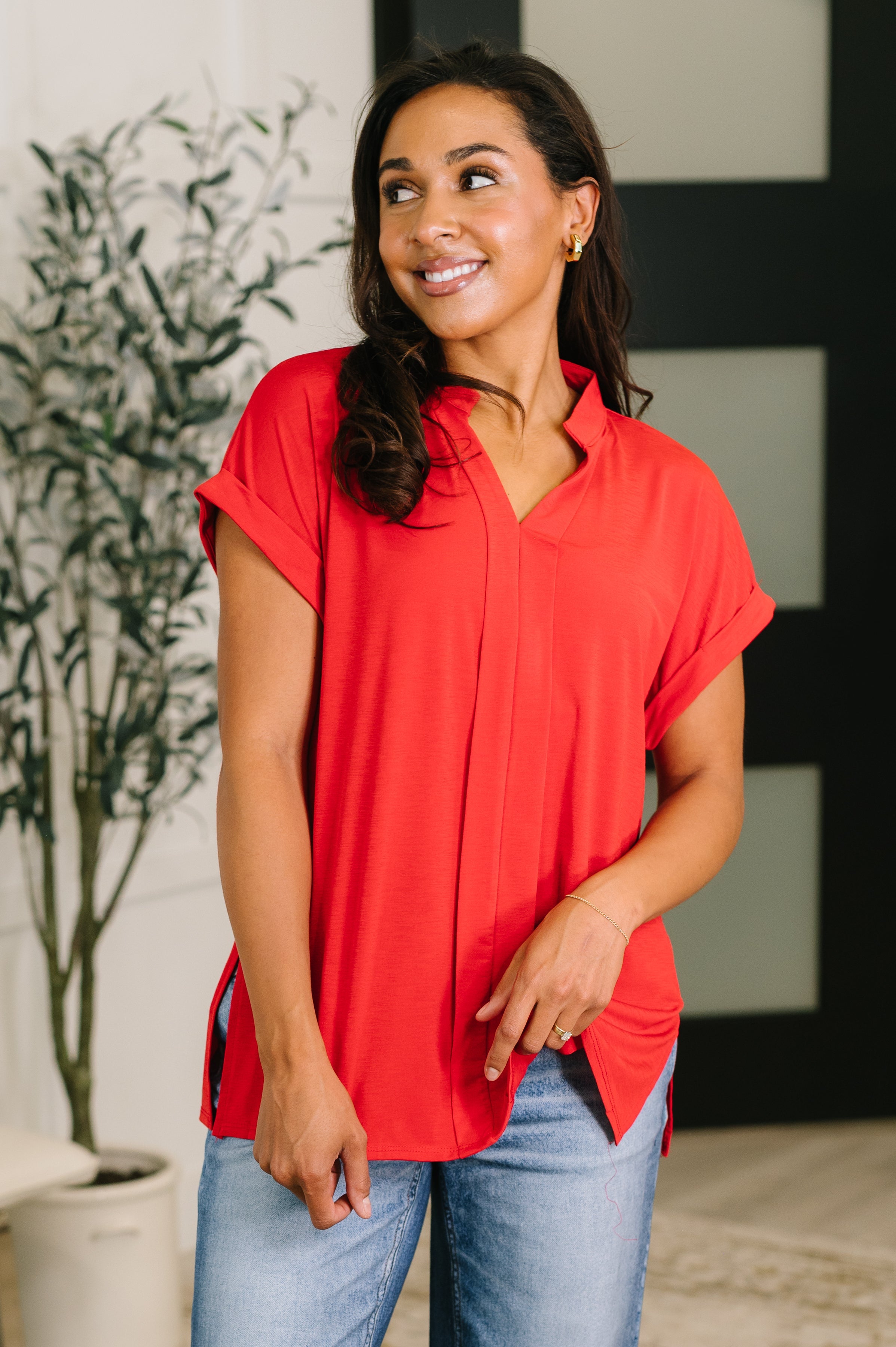 Woman wearing a red split neck blouse with rolled sleeves paired with light blue jeans in a bright indoor setting