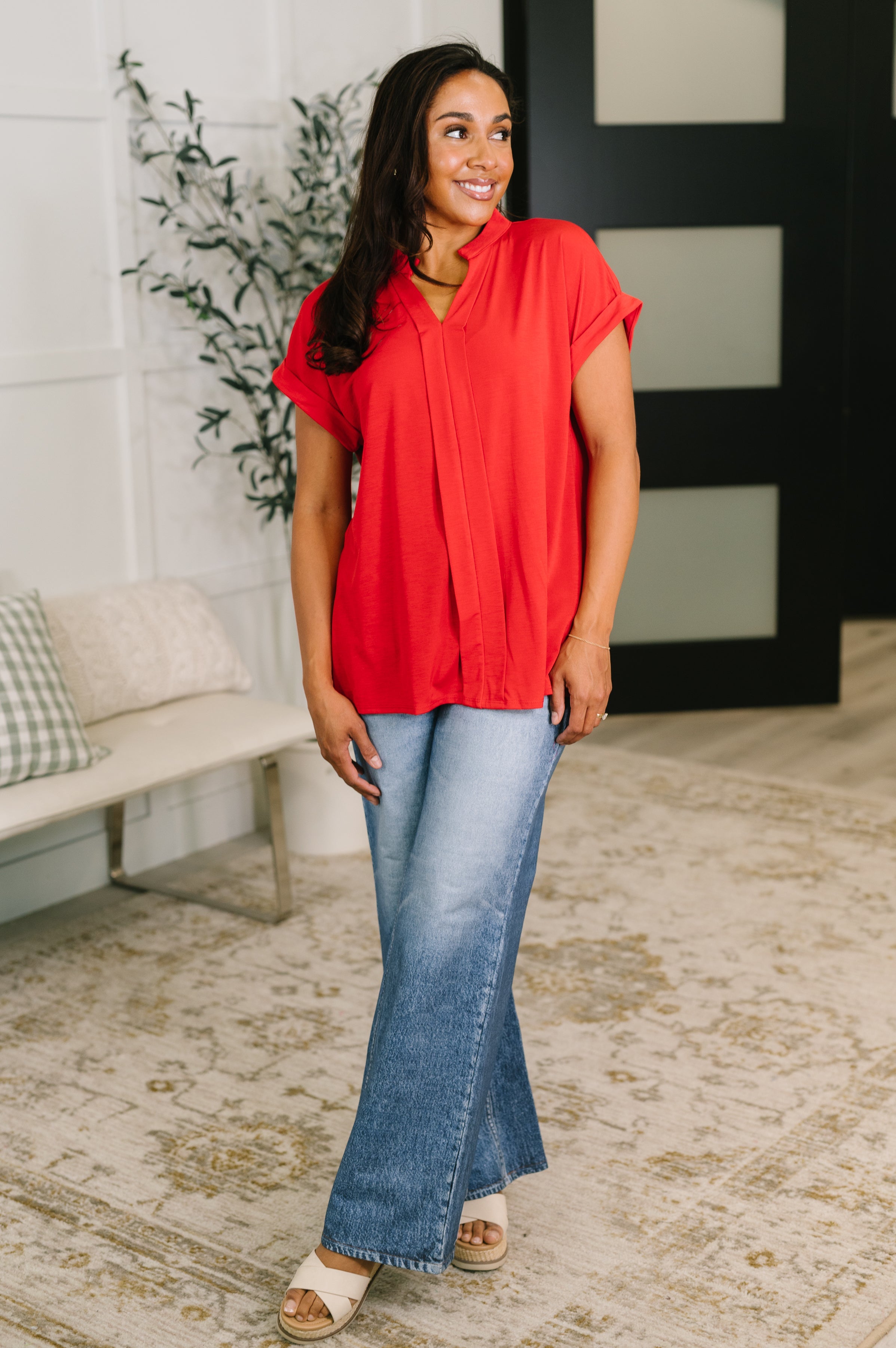 Woman wearing vibrant red split neck blouse paired with light wash wide-leg jeans in cozy indoor setting