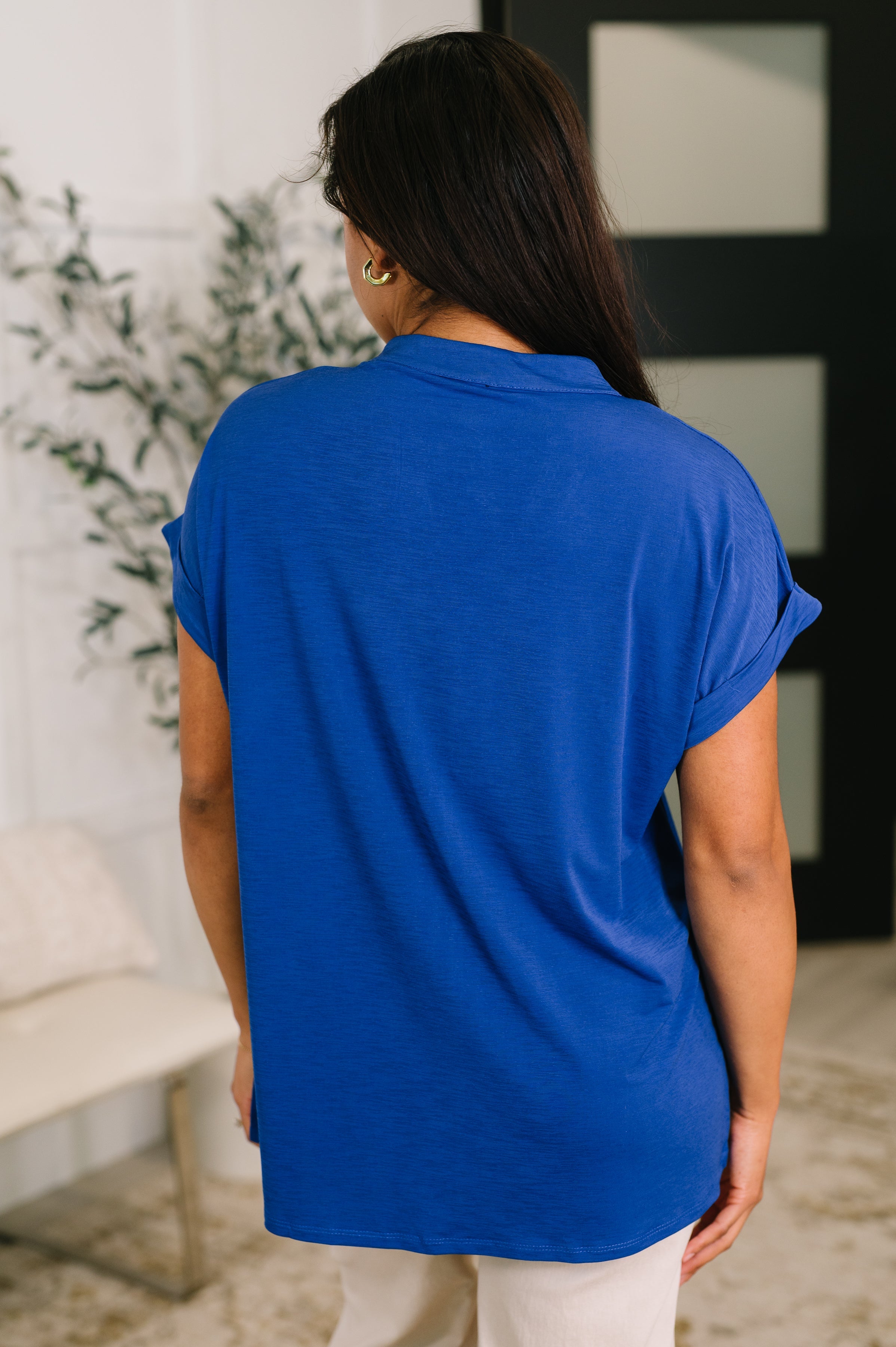 Woman wearing a royal blue relaxed fit blouse with rolled sleeves shown from the back in a cozy indoor setting