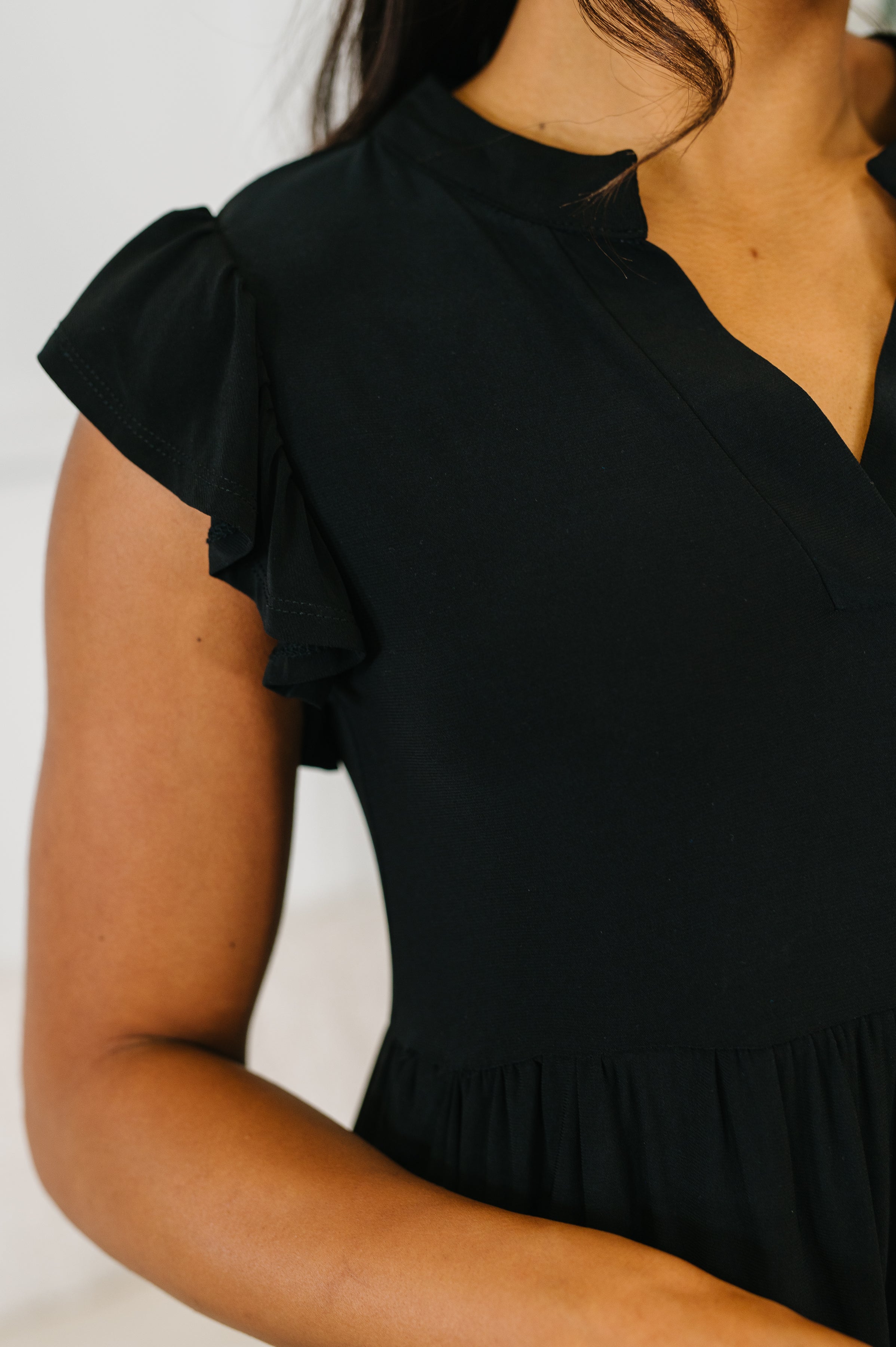 Close-up of black flutter sleeve dress with scalloped neckline and gathered waist on model’s upper body