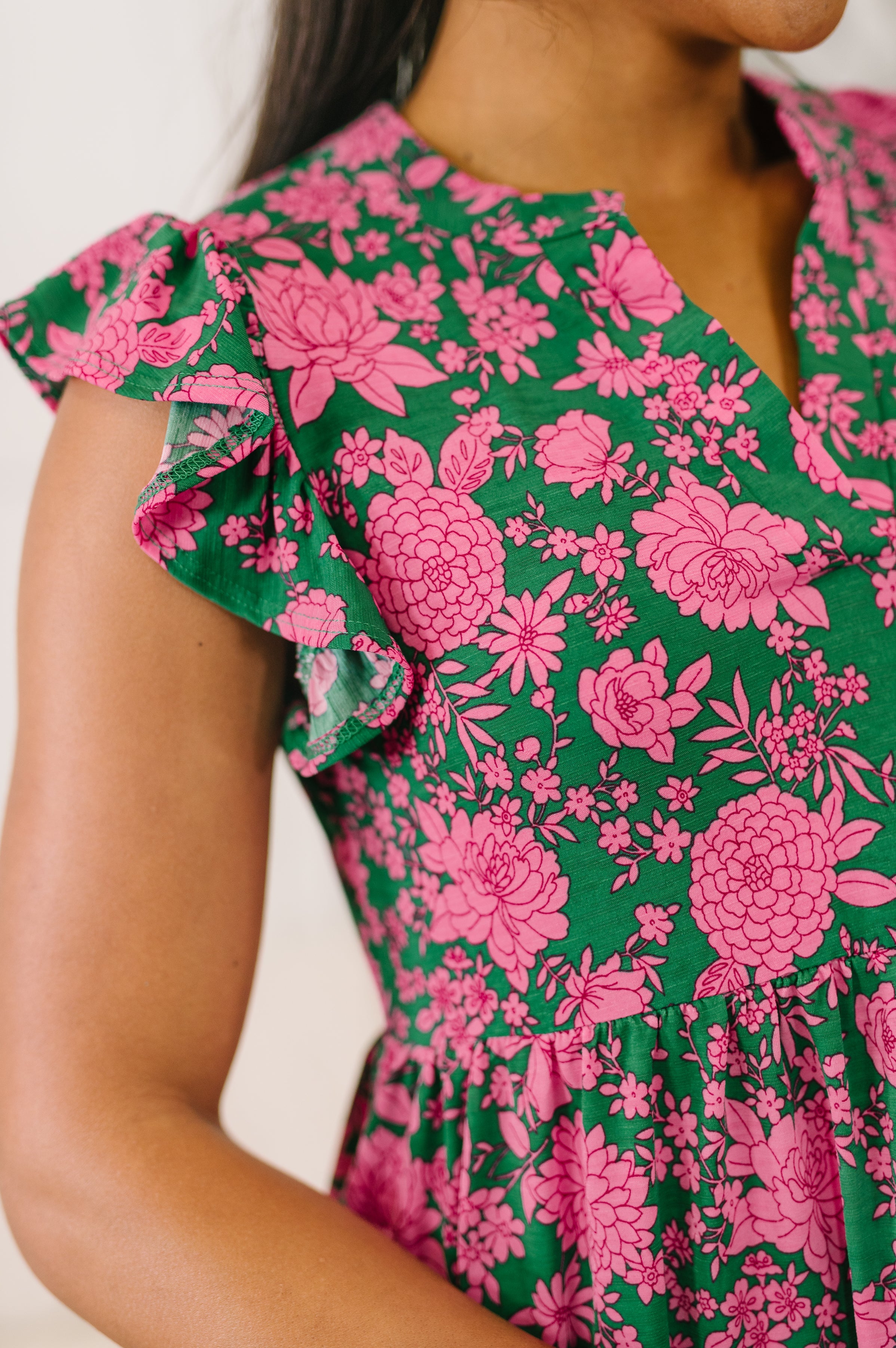 Close-up of woman wearing a green dress with pink floral patterns and short ruffled sleeves