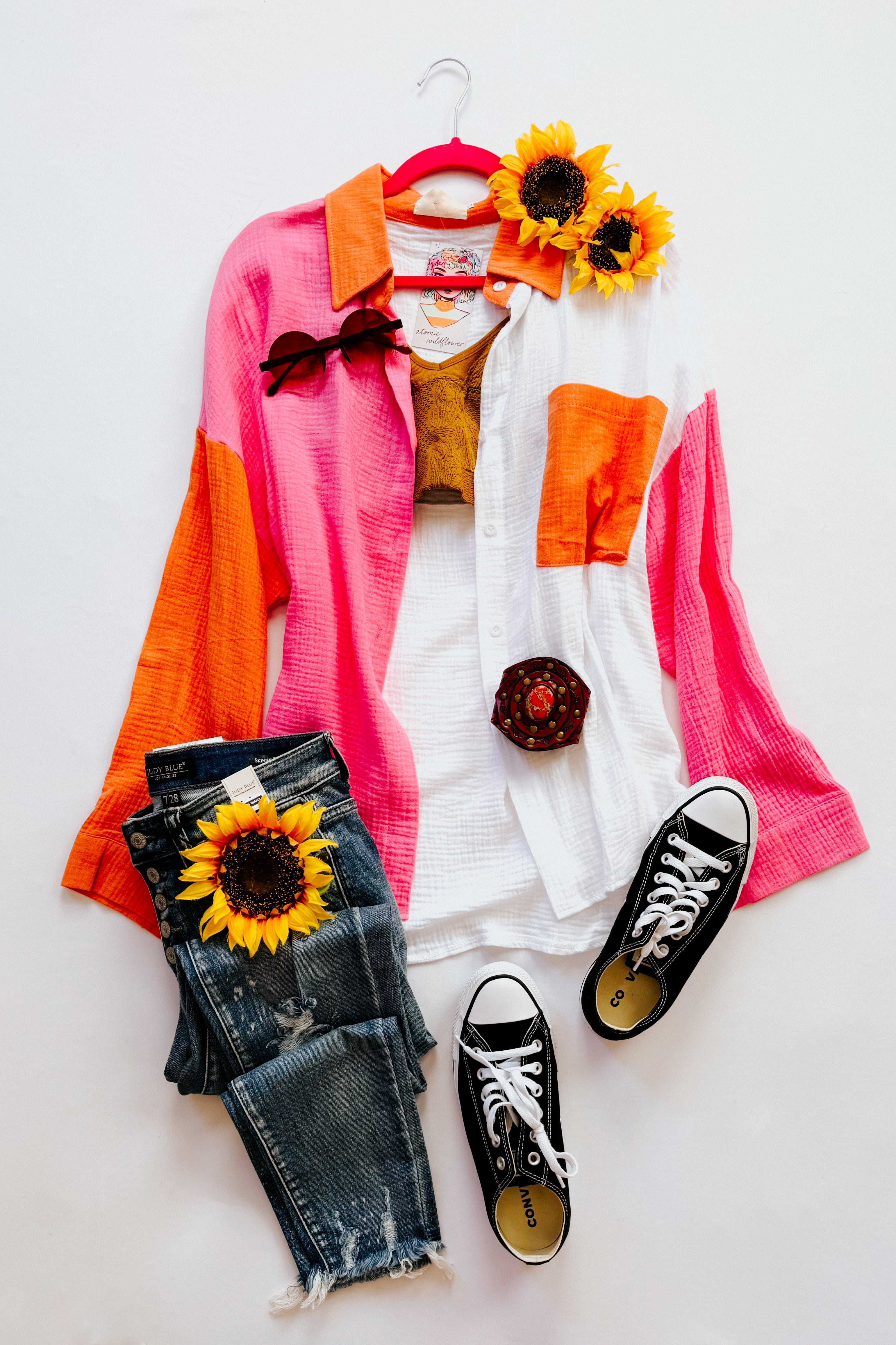 Casual outfit layout with pink, orange, and ivory color block top, distressed jeans, and black sneakers with sunflowers
