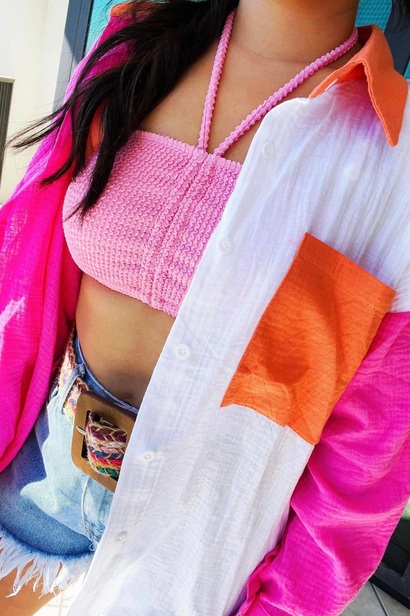 Close-up of woman wearing pink smocked crop top and white shirt with pink sleeves and orange pocket paired with denim shorts