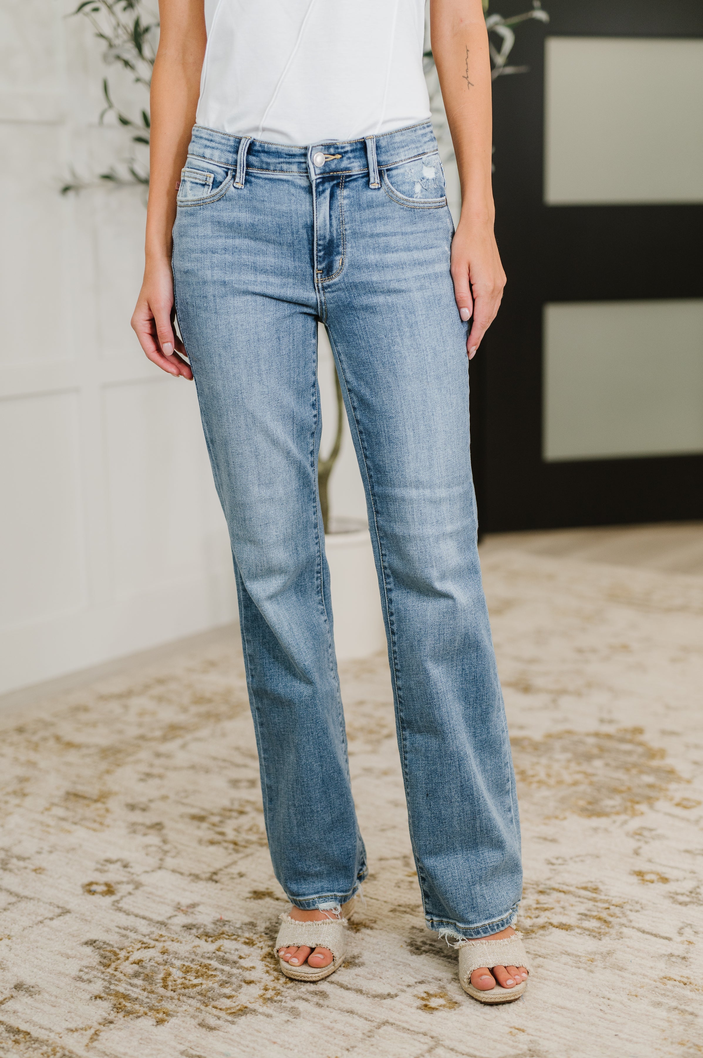 Woman wearing mid-rise blue denim jeans with slight fading and raw hem paired with white top and open-toe sandals