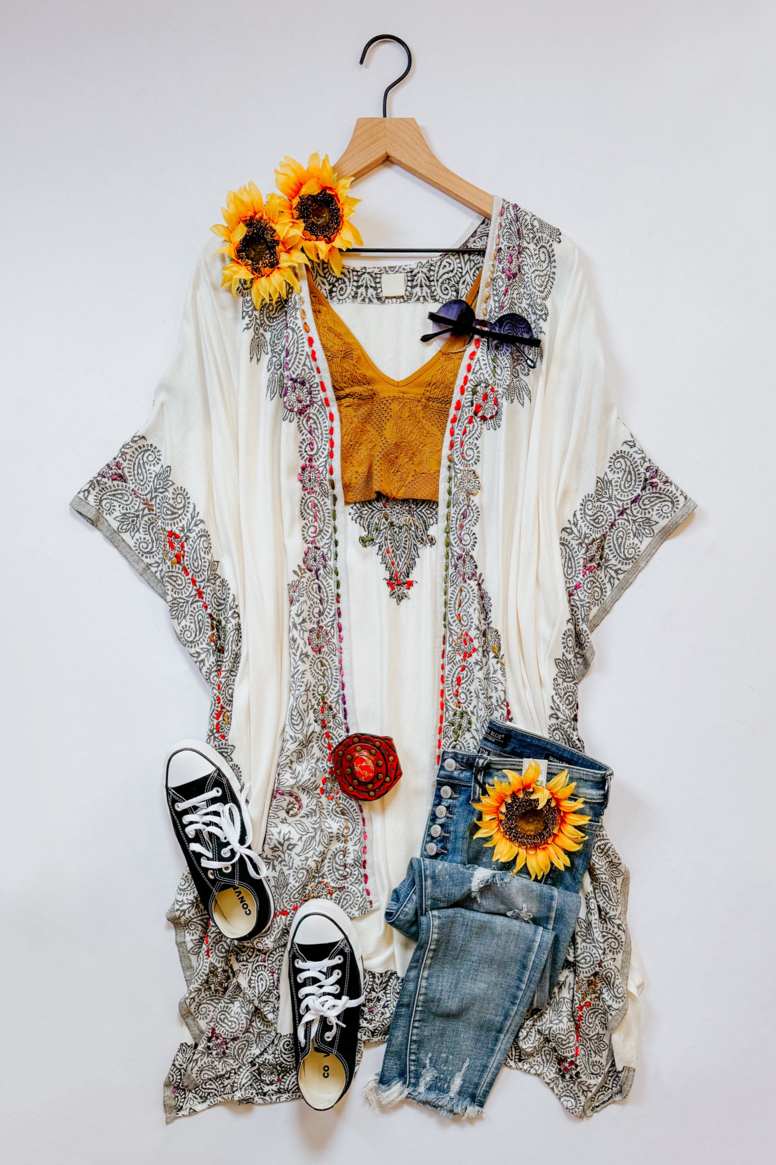 Ivory and black patterned duster with mustard top, distressed blue jeans, black sneakers, and sunflower accents on white background