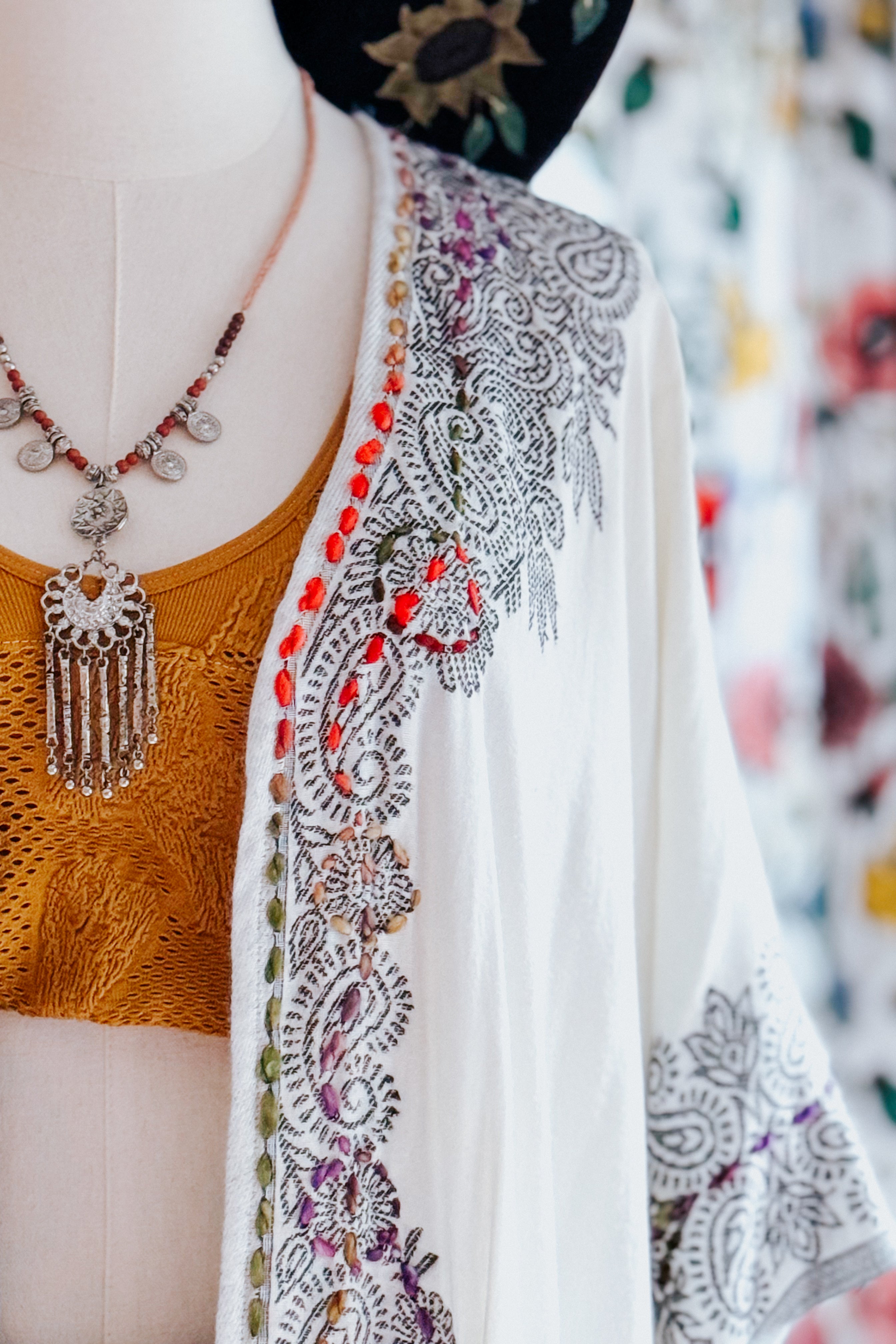 Close-up of ivory and black patterned duster with colorful embroidered trim layered over mustard textured top on mannequin