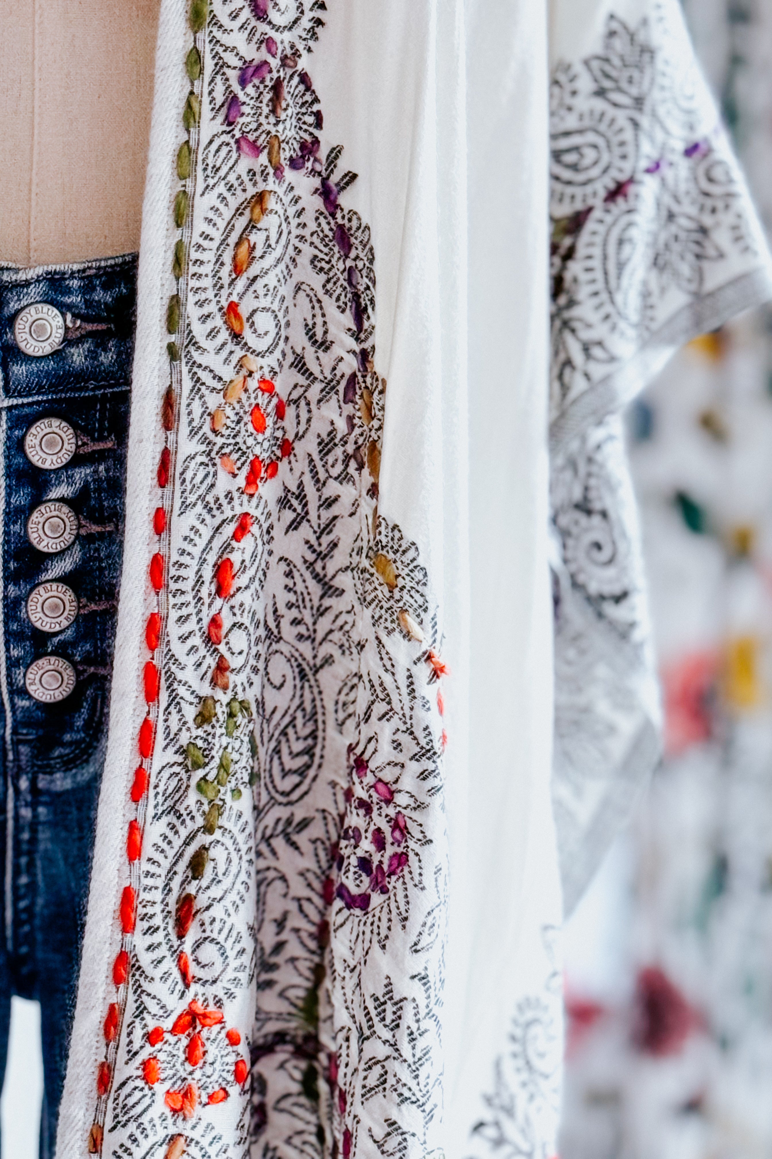 Close-up of ivory and black patterned fabric with colorful embroidered floral accents paired with button-fly denim jeans