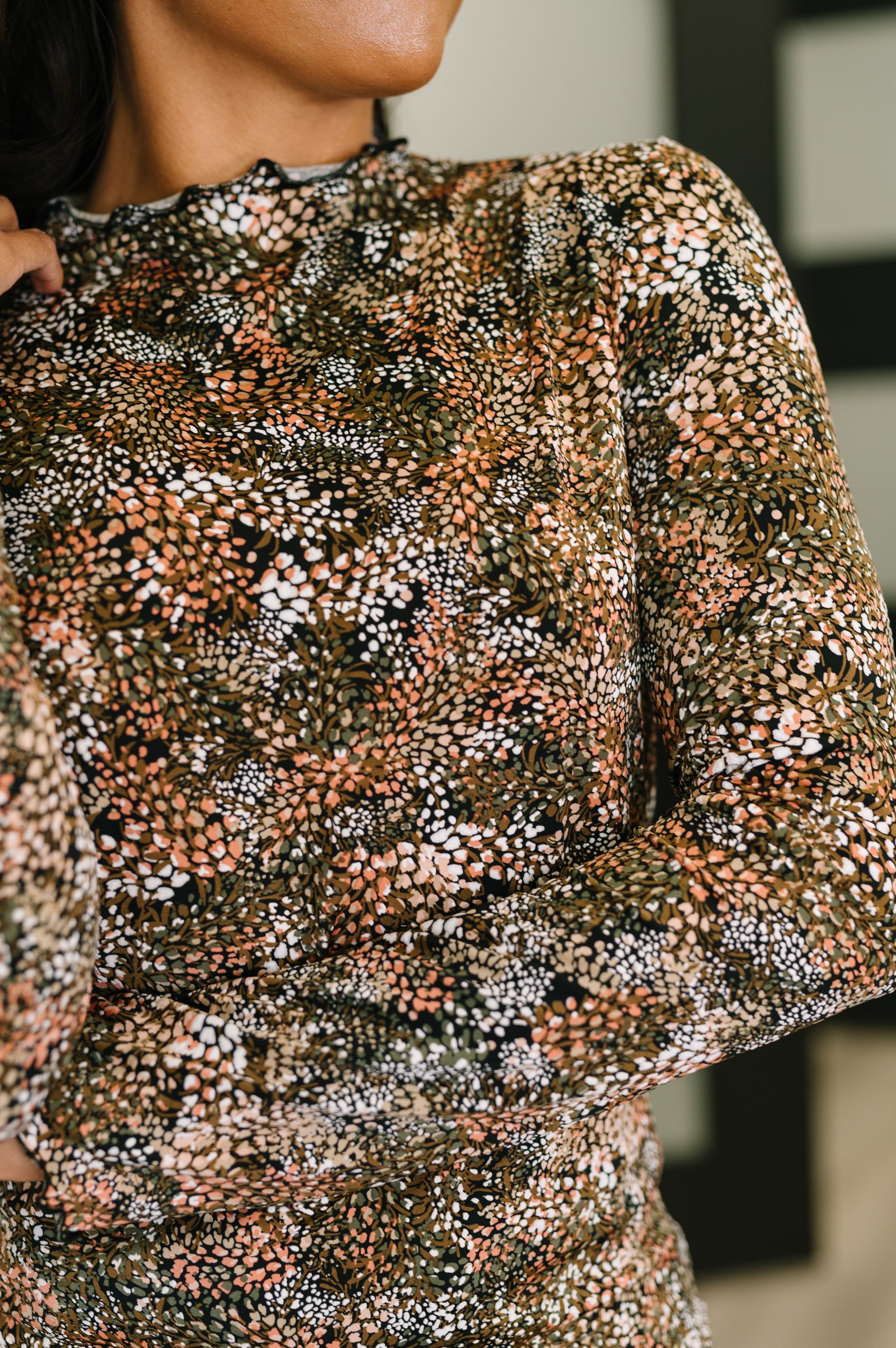 Close-up of a woman wearing a long-sleeve top with a multicolor abstract pattern in earthy tones and soft ruffle neckline