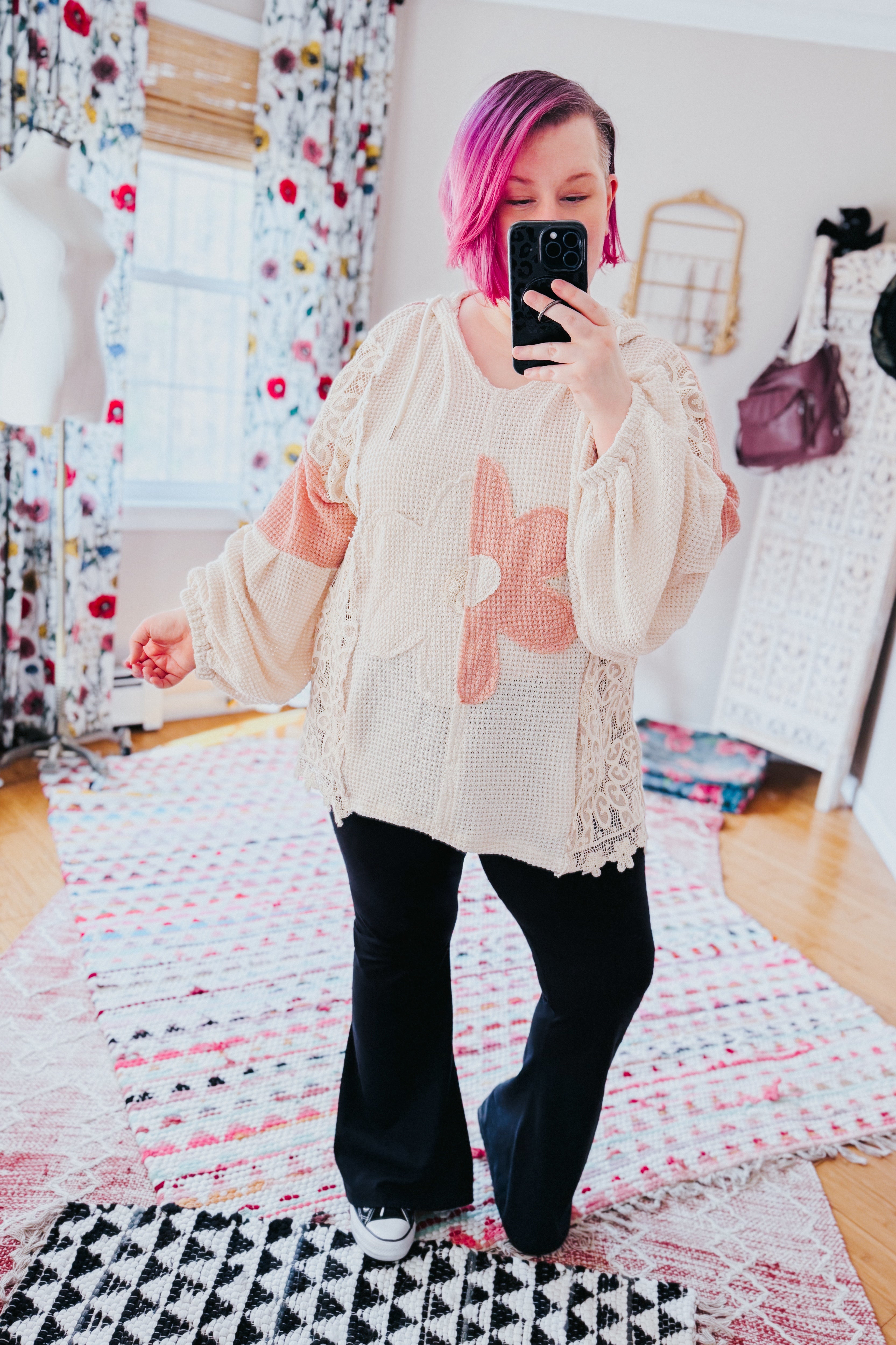 Woman wearing cream waffle knit top with peach floral appliqués and lace side panels paired with black flared pants