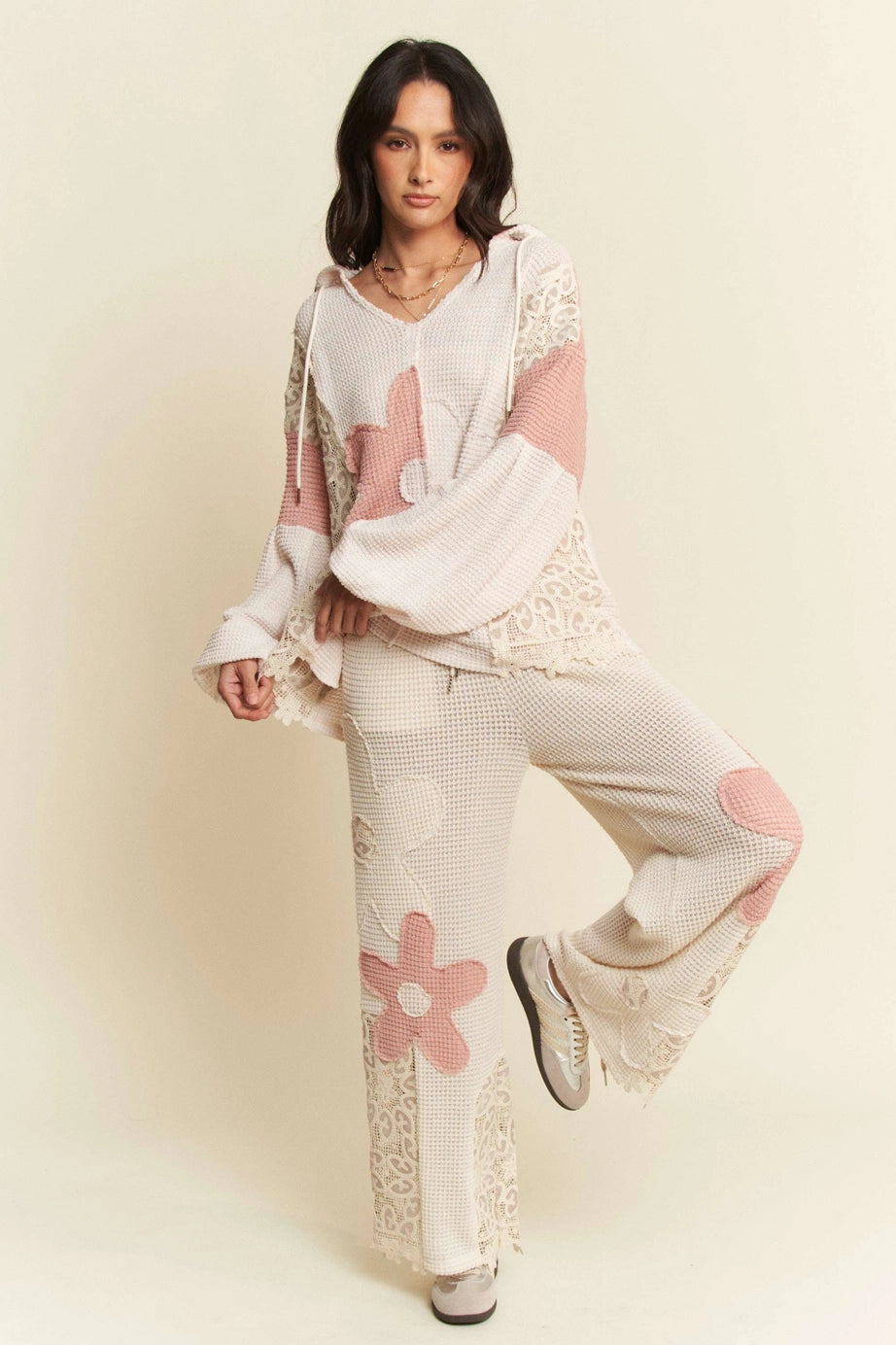 Woman wearing cream waffle knit loungewear with pink floral patches and lace accents posing against neutral backdrop