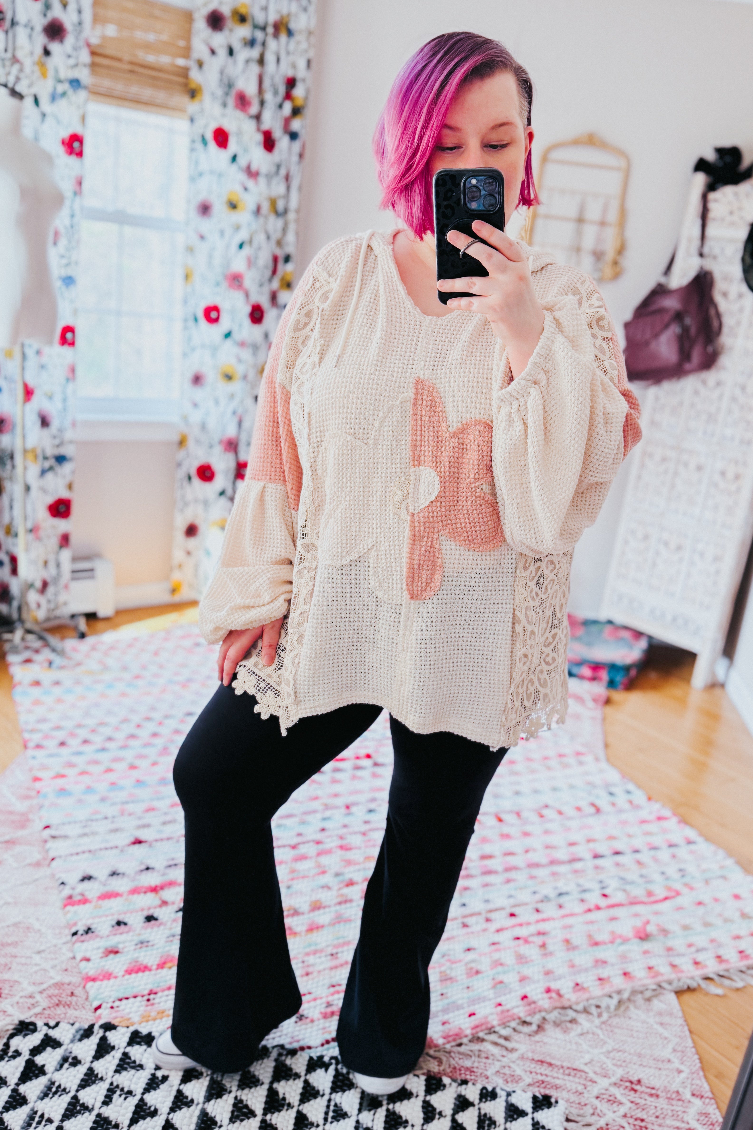Loose cream waffle knit pullover with blush floral appliqué and lace inserts worn with black pants in bright room
