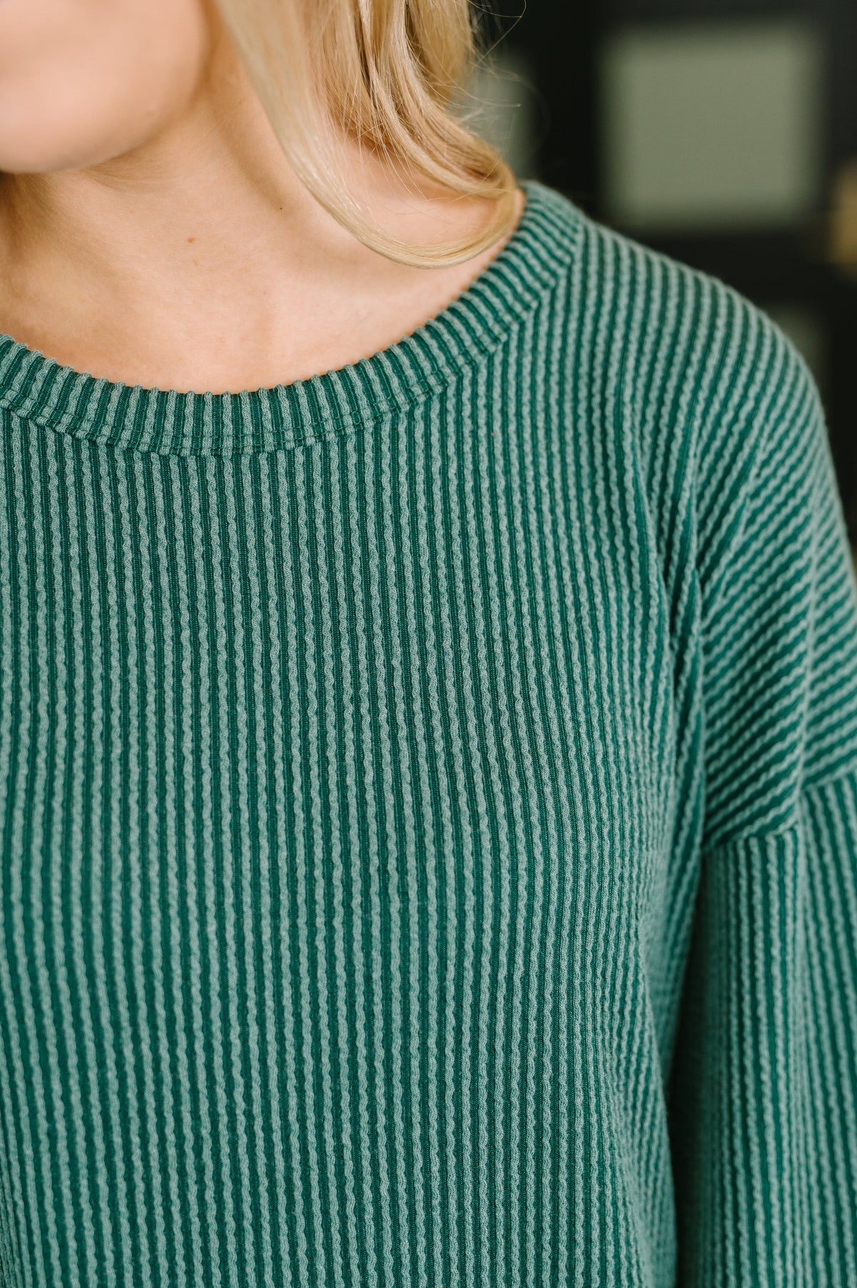 Close up of a green textured knit dress featuring vertical ribbing, a banded round neckline, and long sleeves