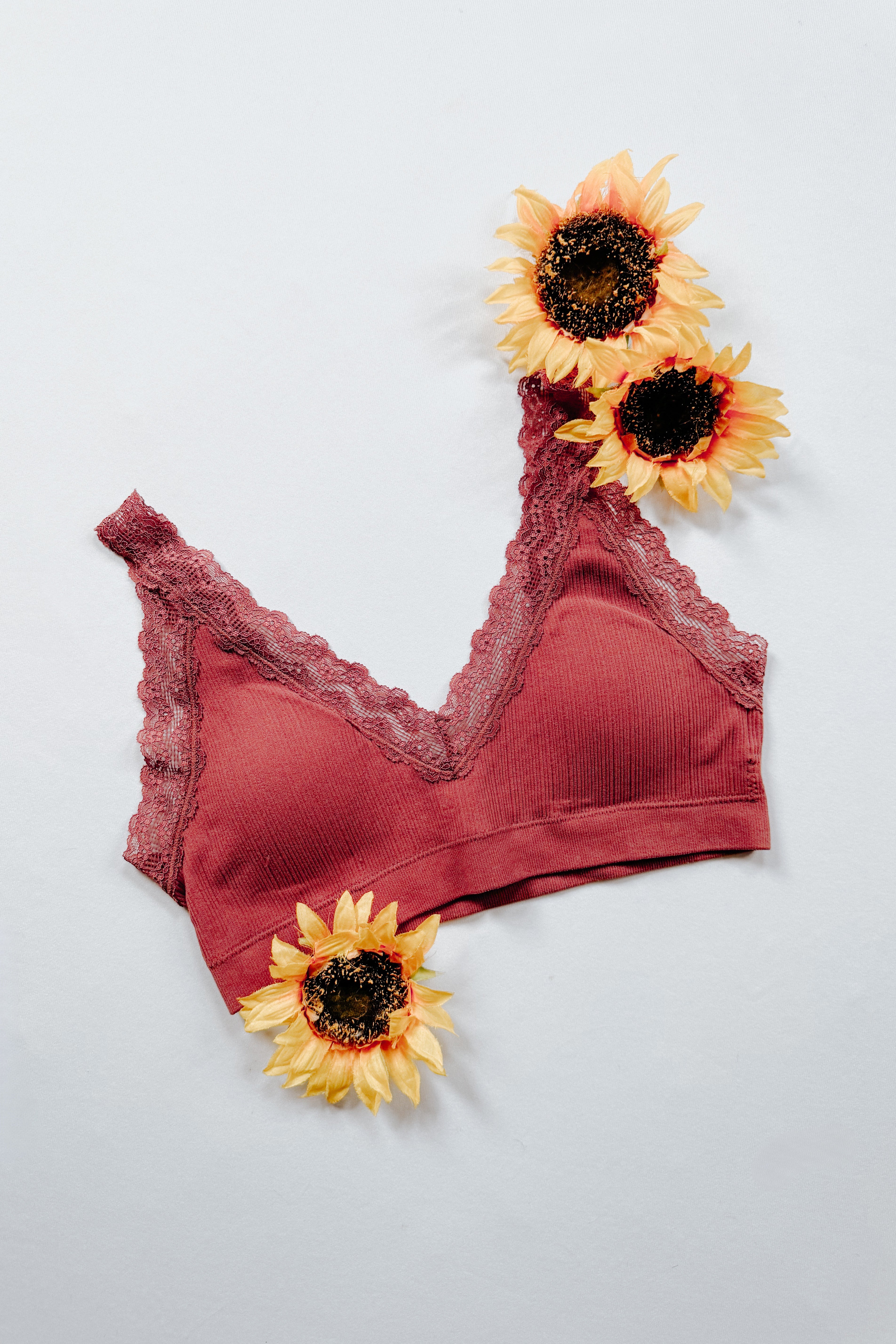 Rust-colored ribbed bralette with delicate lace trim displayed flat with decorative sunflowers on light background