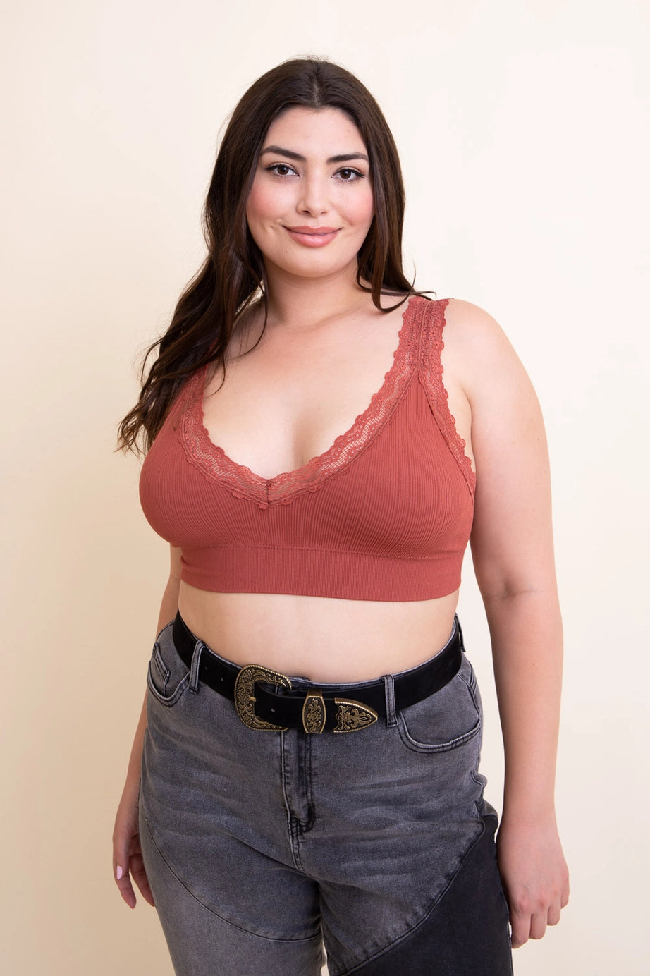 Curvy woman wearing rust-colored ribbed bralette with lace trim paired with two-tone gray jeans and black belt