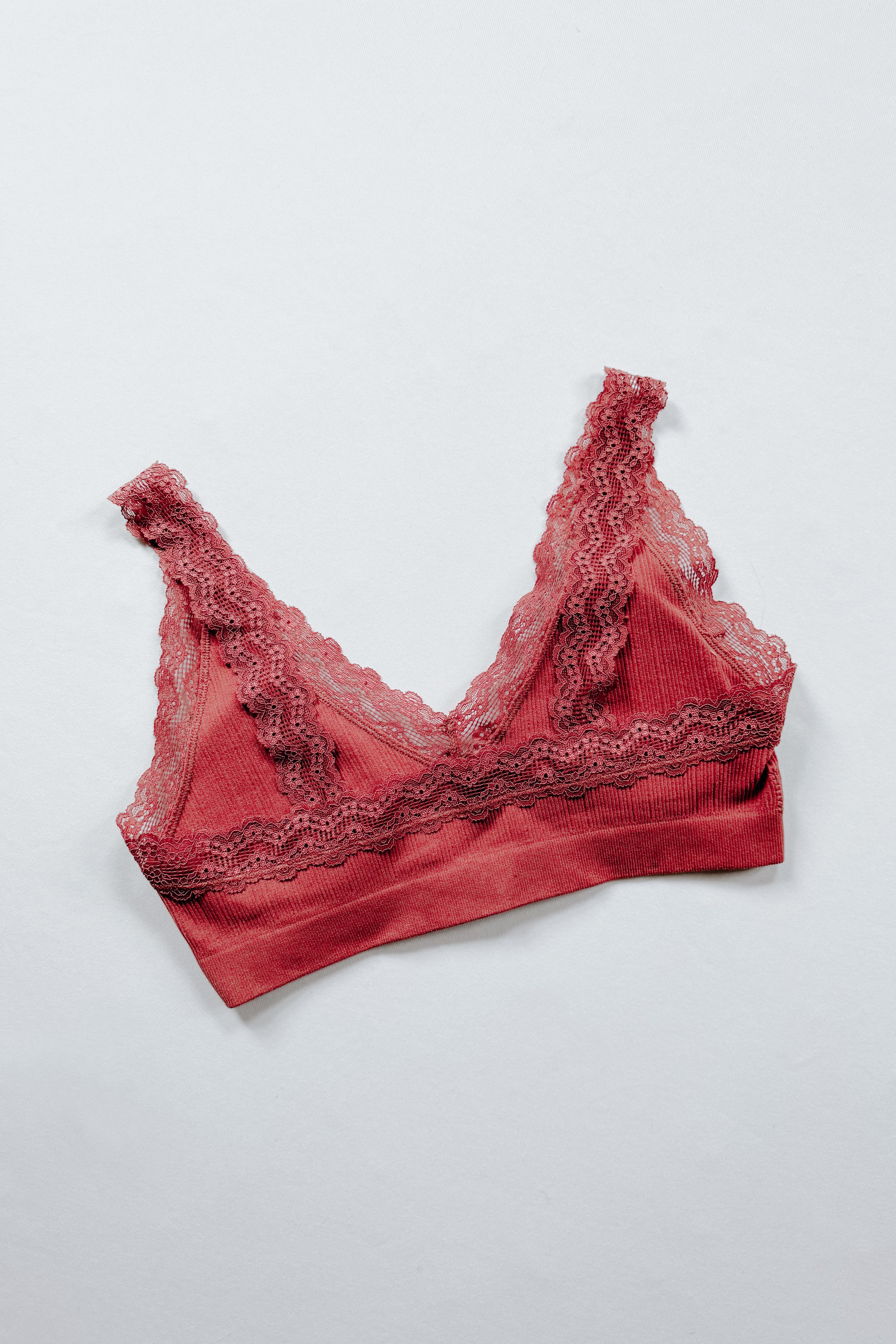 Rust-colored ribbed bralette with intricate floral lace trim along the neckline and band displayed on light surface
