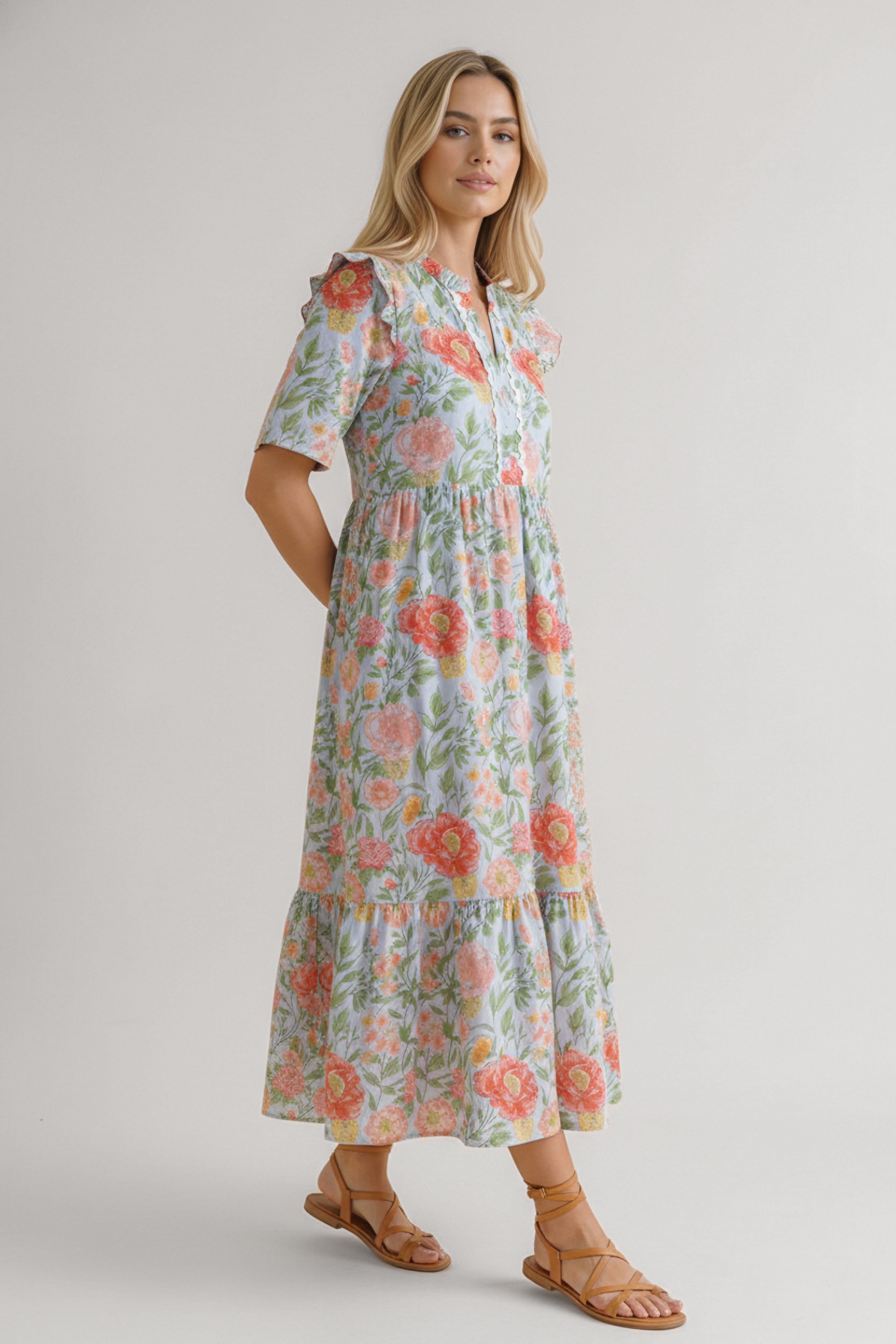 Woman wearing floral midi dress with ruffled sleeves and tiered skirt paired with strappy sandals against neutral background