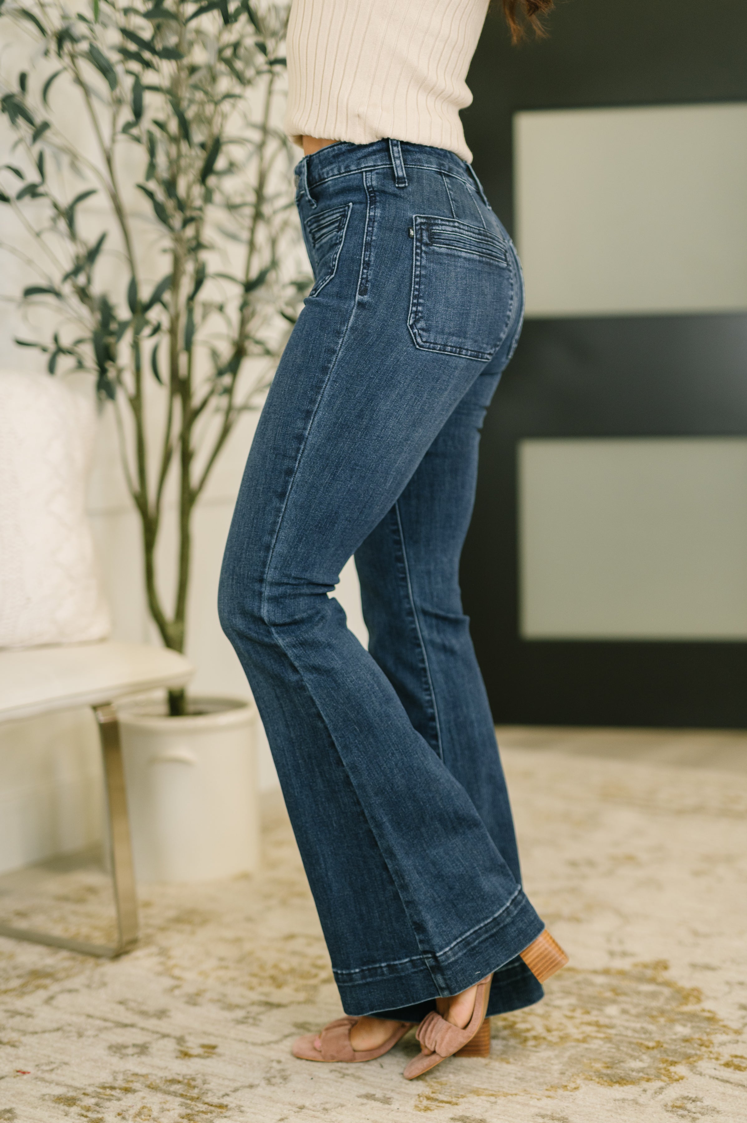 Side profile of woman wearing Mackenzie high waist flare jeans with vintage pockets indoors on carpeted floor