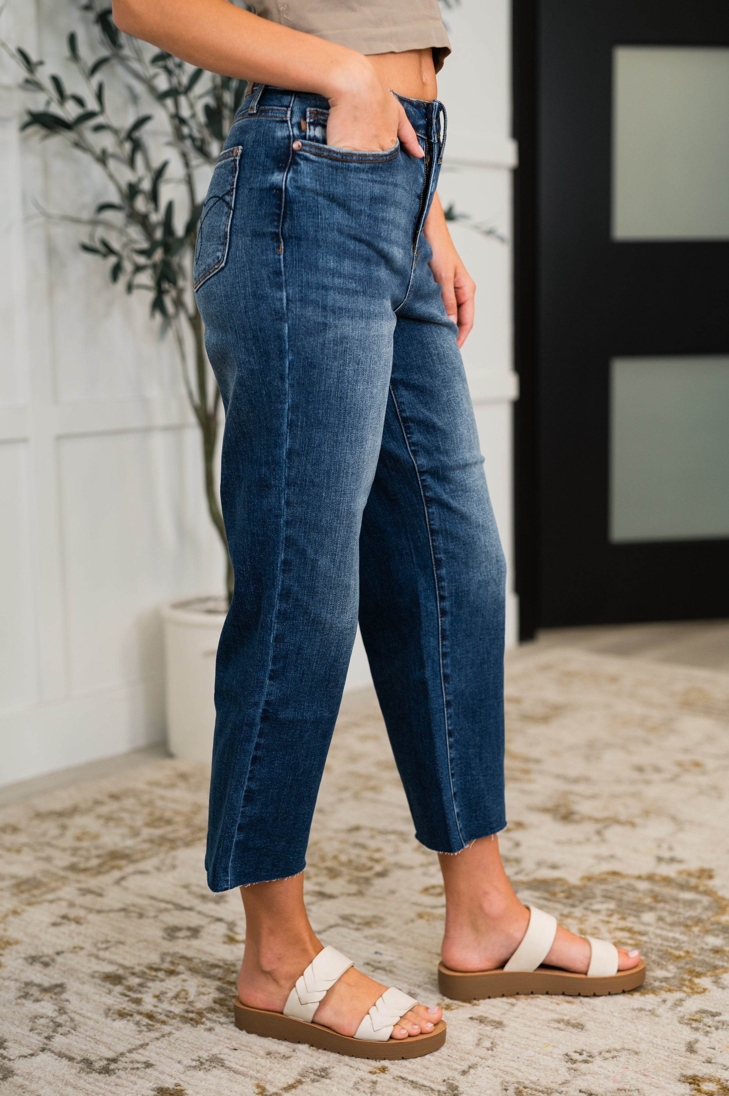 Woman wearing high-rise blue denim straight-leg jeans with raw hem and white double-strap sandals indoors