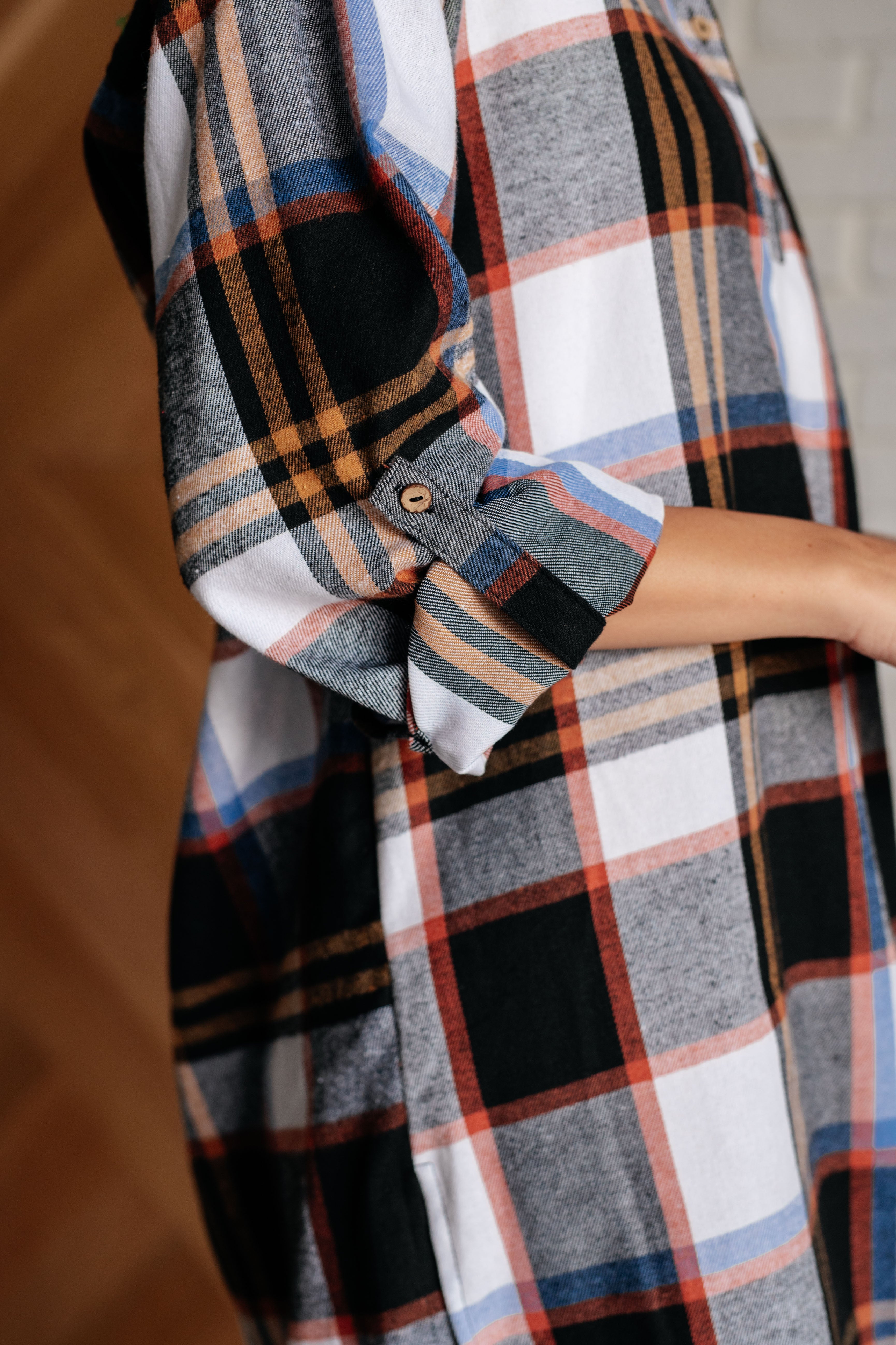 Close-up of a rolled-up sleeve on a black plaid shirt dress with tan, blue, and rust accents indoors