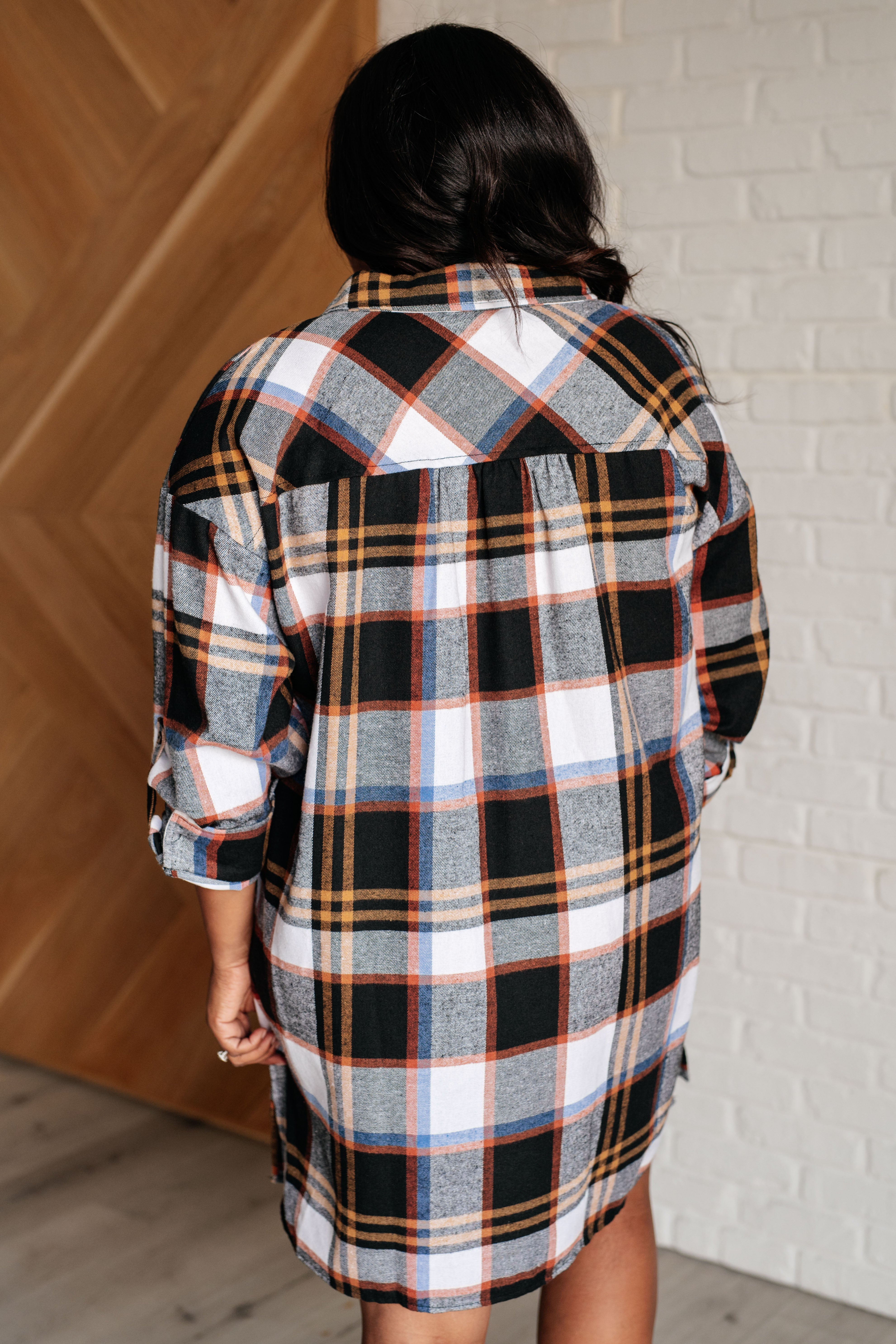 Rear view of a woman wearing a black plaid shirt dress with orange, white, and blue details indoors