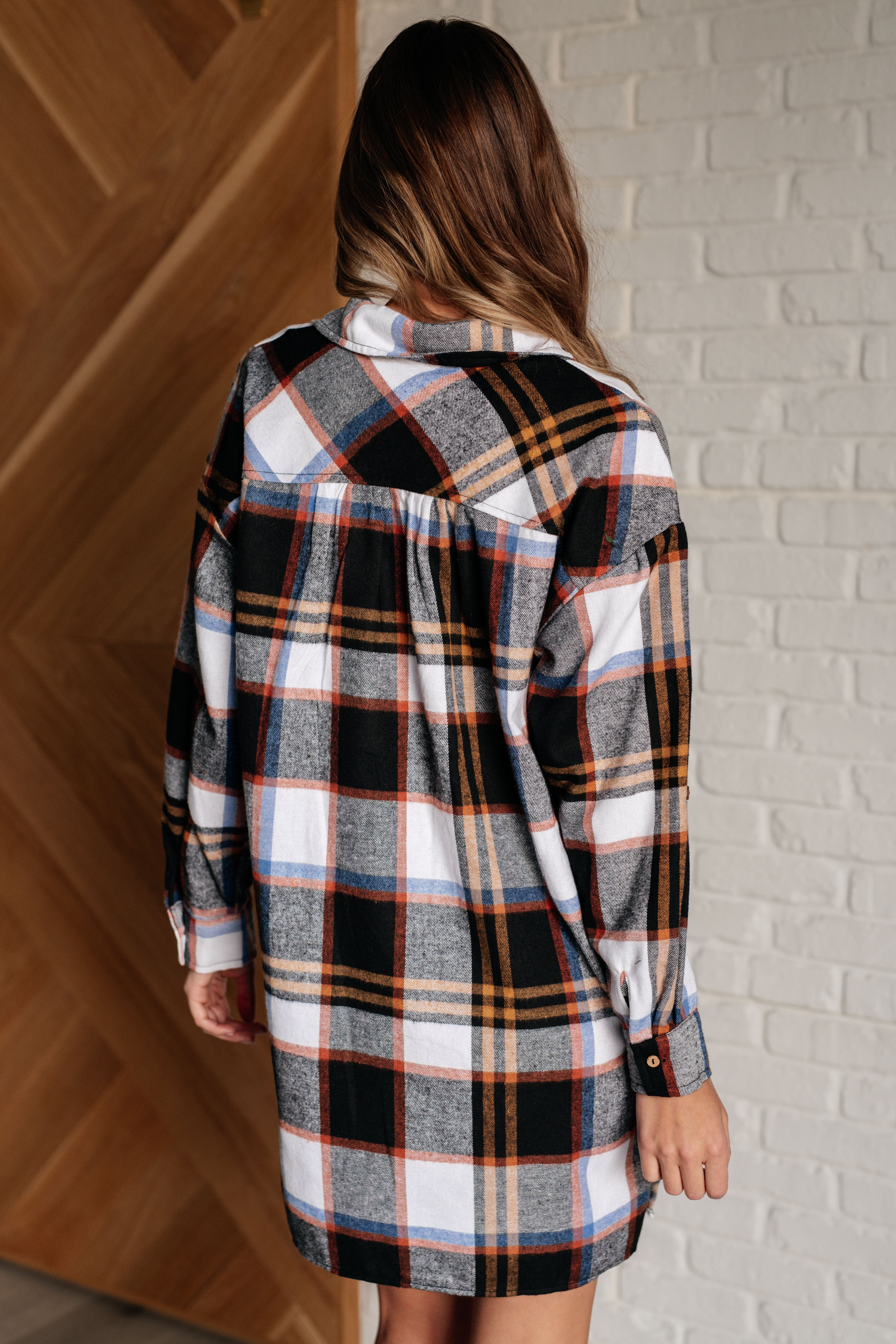 Back view of a woman wearing a black plaid shirt dress with orange, gray, and white details indoors