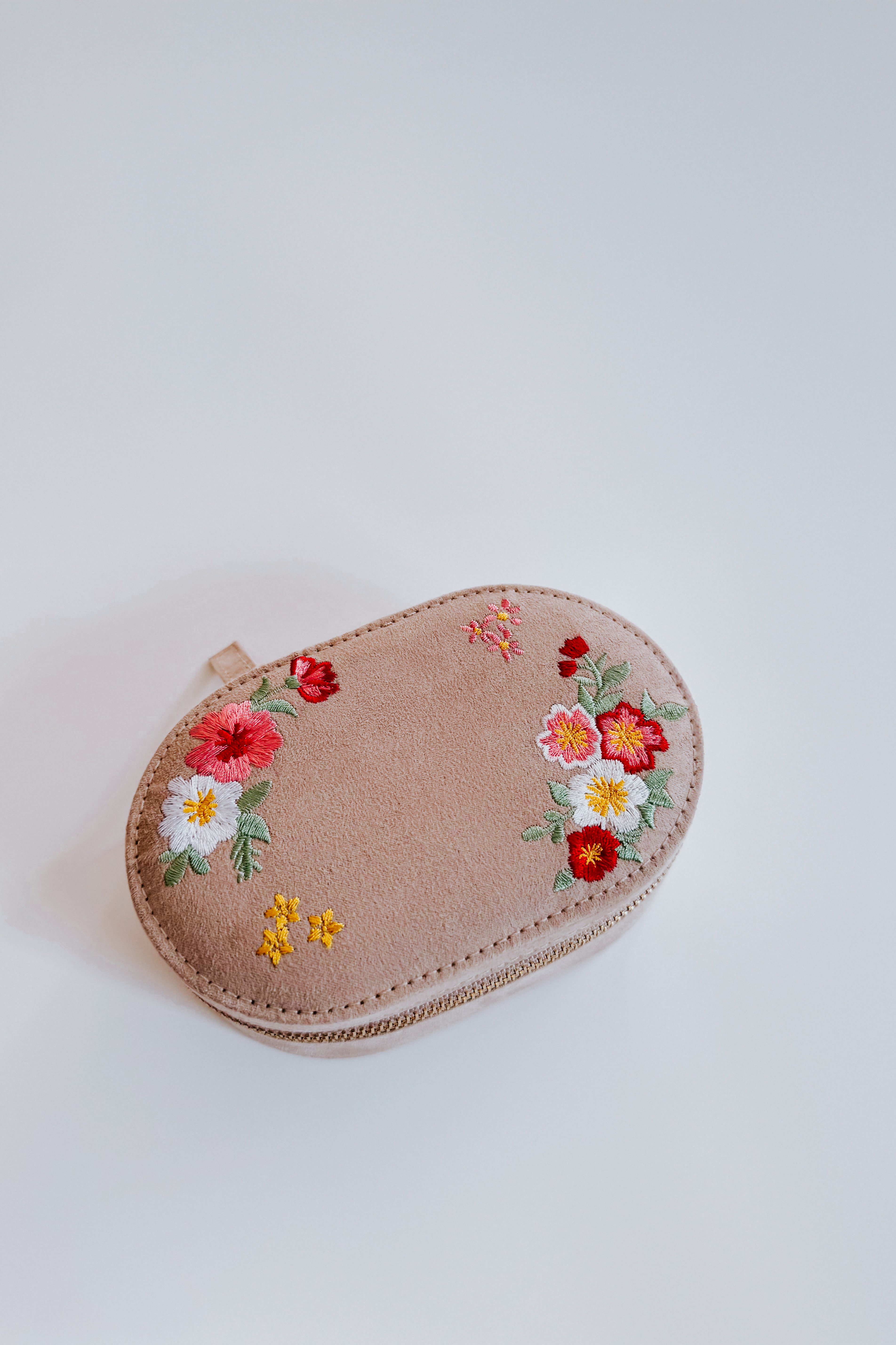 Cream velvet jewelry case with colorful floral embroidery and stitched edges on a light surface