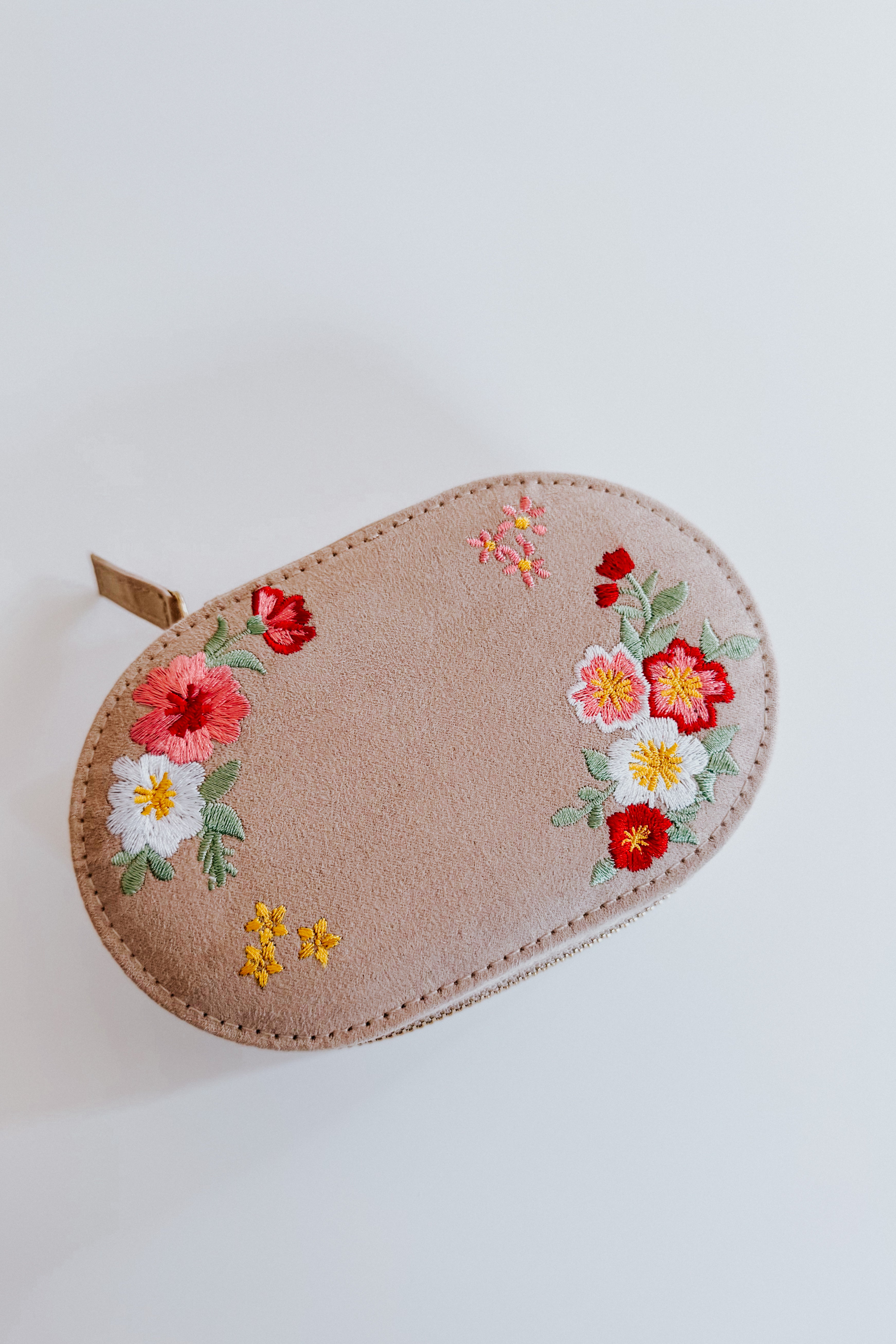 Oval cream velvet jewelry case with colorful floral embroidery on a plain white background