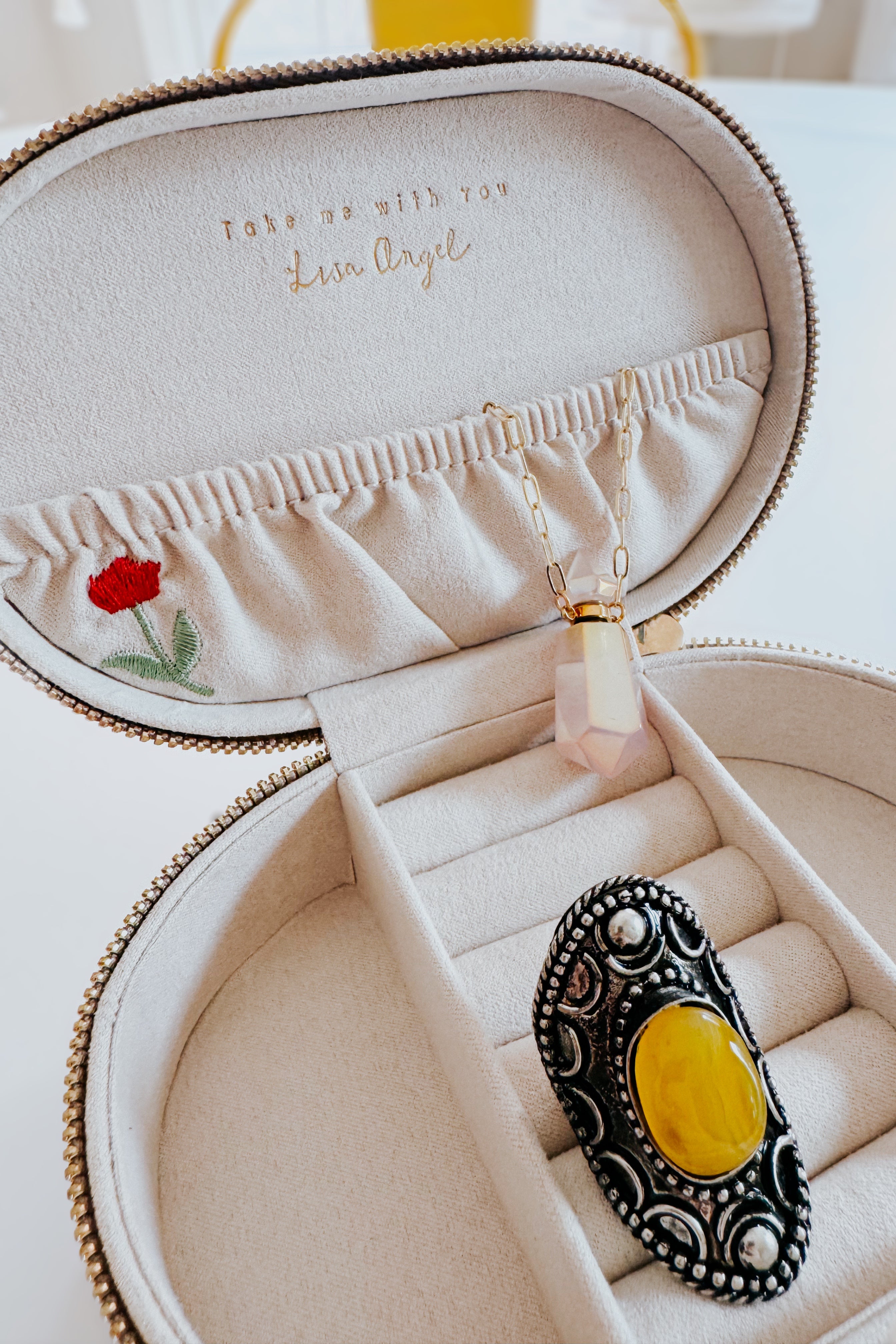 Cream velvet jewelry box with floral embroidery holding a gold chain necklace and ornate ring on soft fabric interior