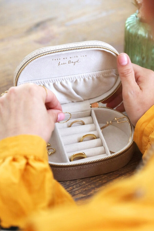 Hands holding an open cream velvet jewelry organizer with gold rings inside on a wooden surface