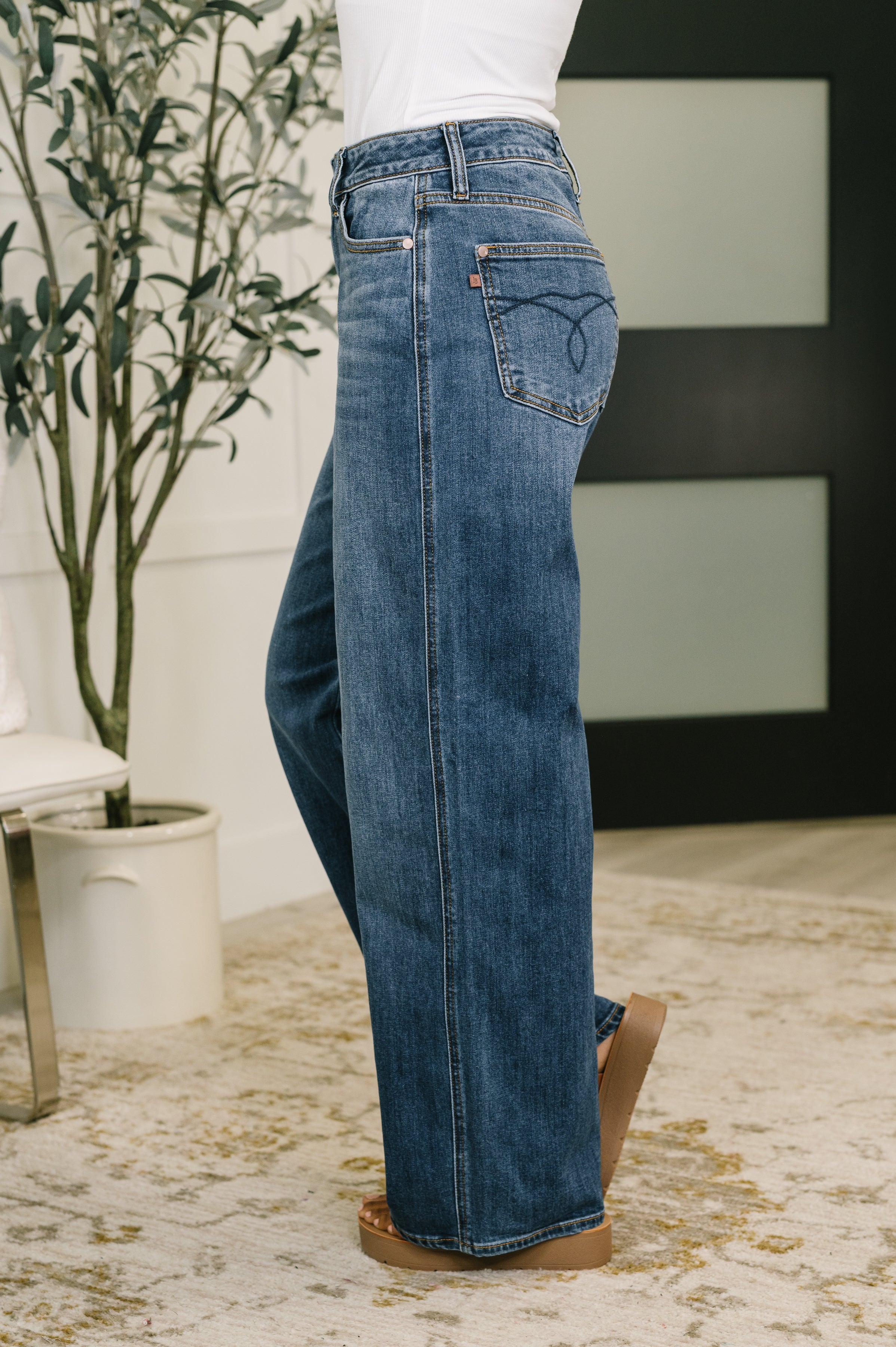 Side view of model wearing high waist baggy blue jeans with stitched back pocket detail indoors