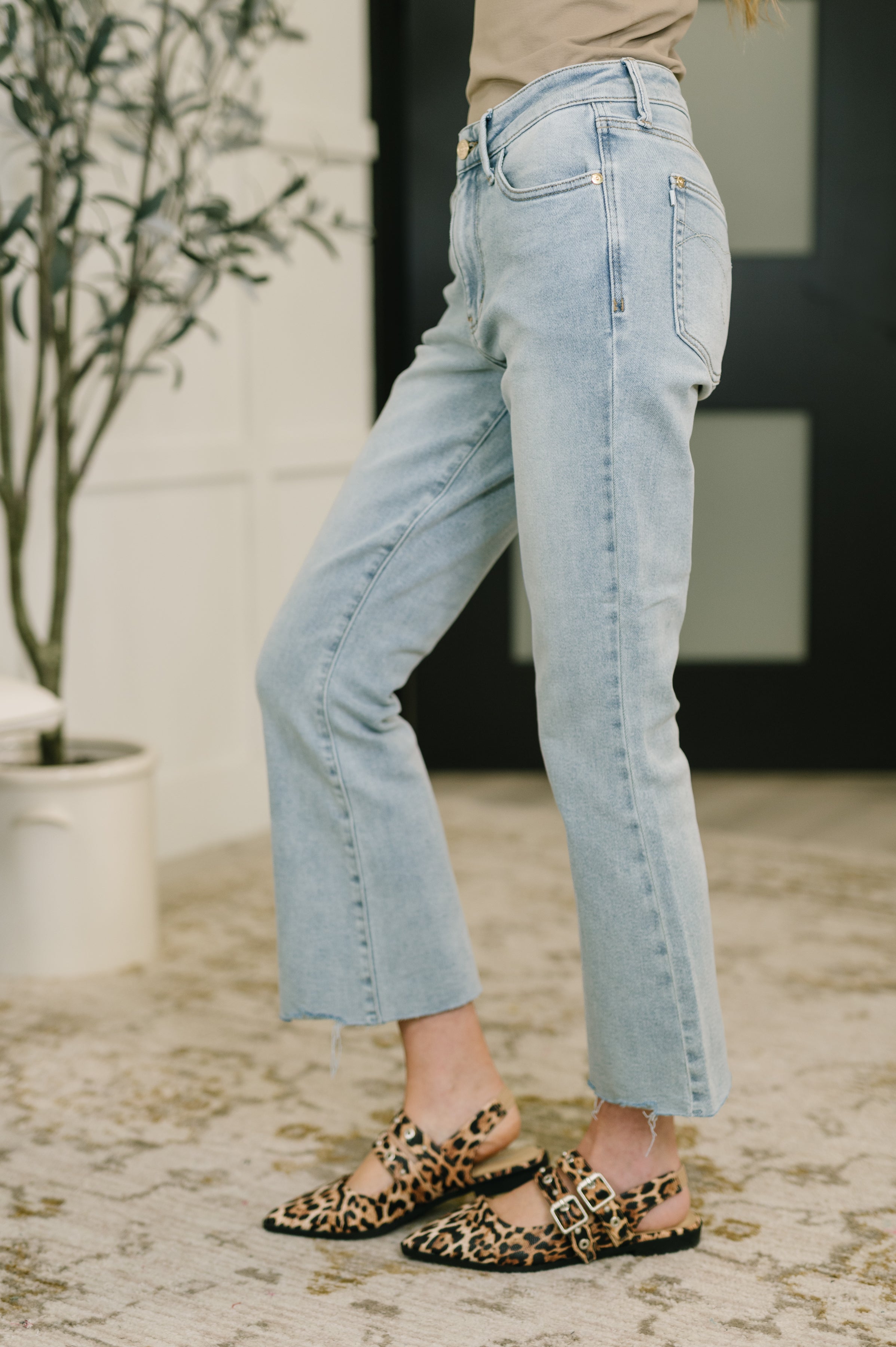 Light wash mid-rise kick flare jeans with unfinished raw hems worn with leopard print buckle flats indoors