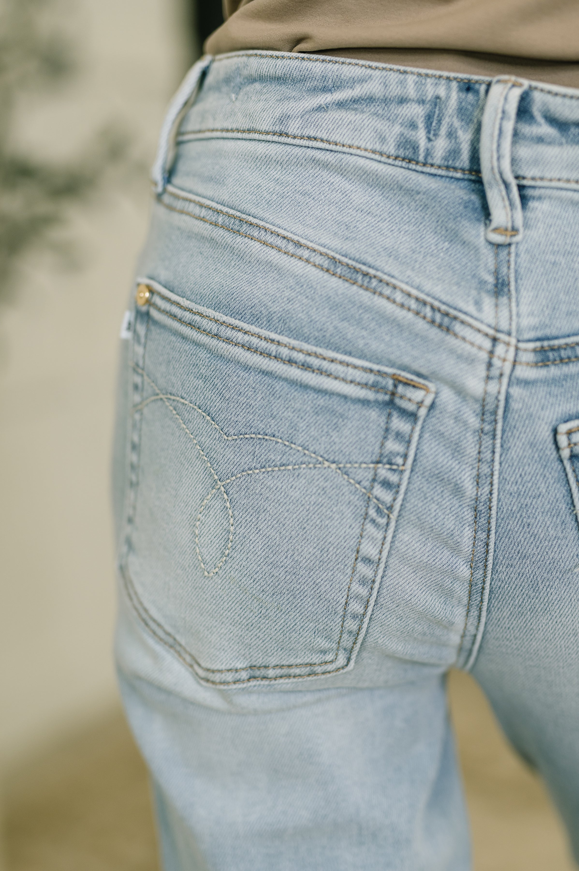 Close-up of light wash mid-rise denim jeans with detailed stitching on back pocket and raw hem visible