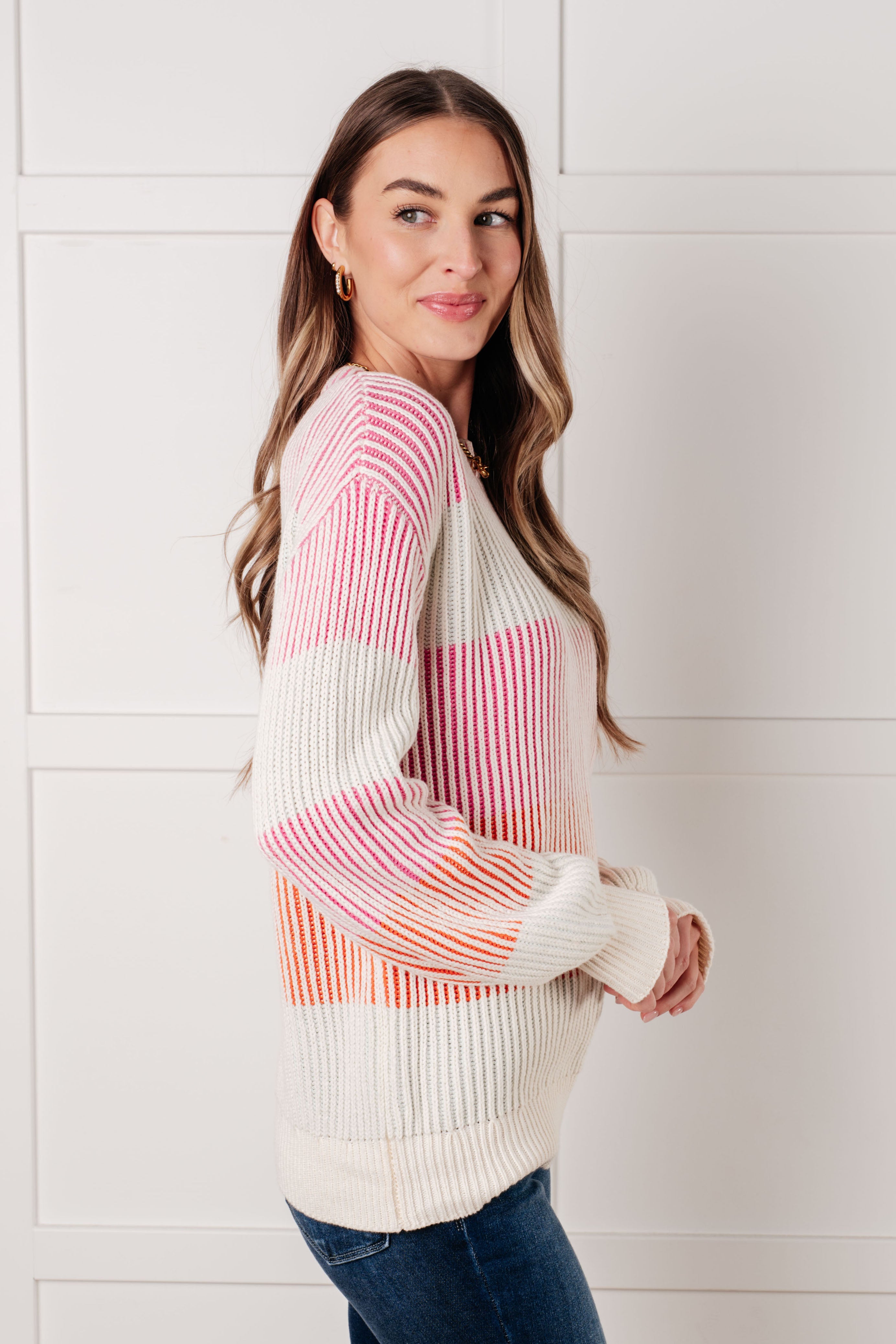 Woman wearing a pink striped ribbed knit top with long sleeves paired with dark blue jeans indoors