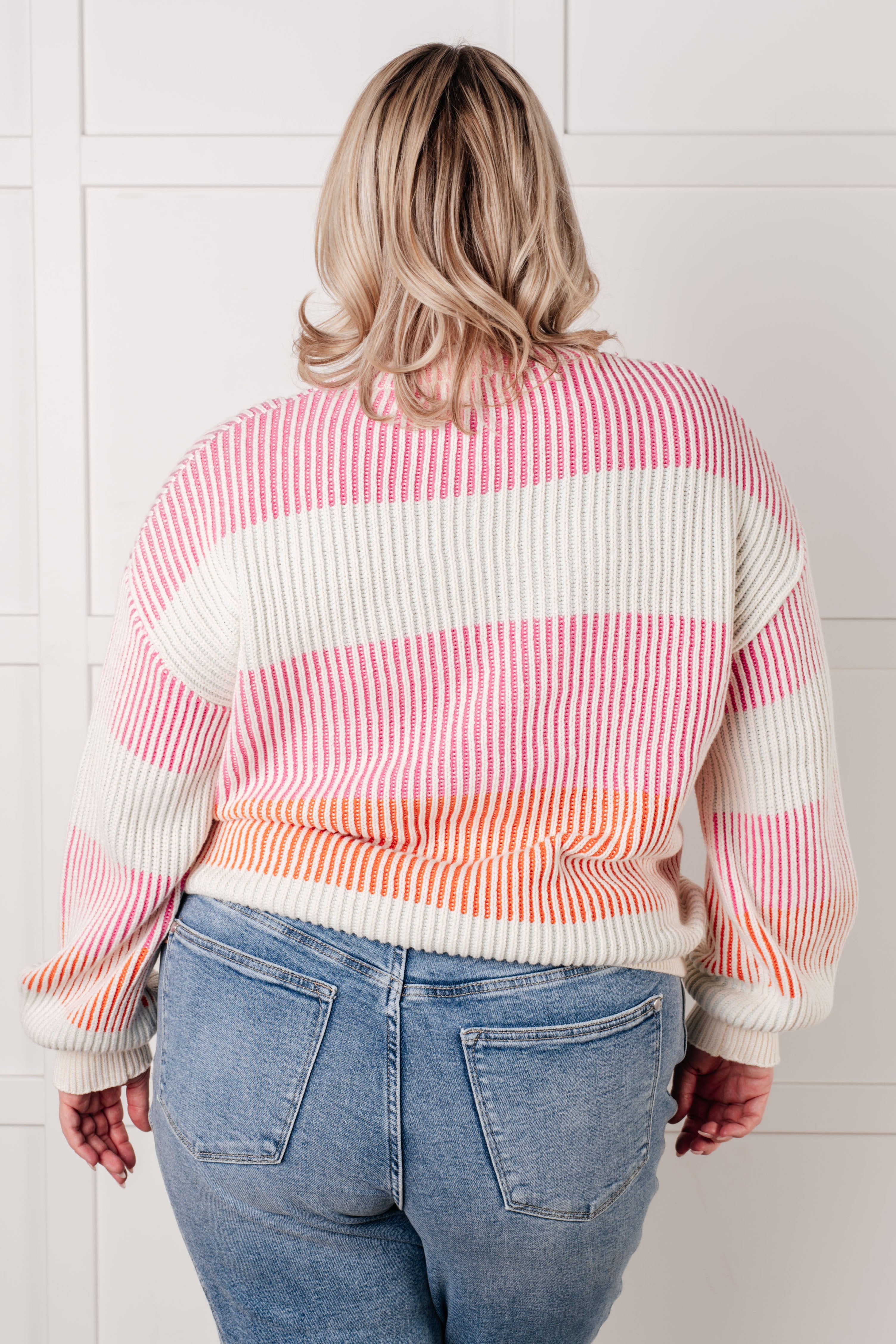 Back view of ribbed sweater with pink and orange stripes worn with light blue jeans indoors