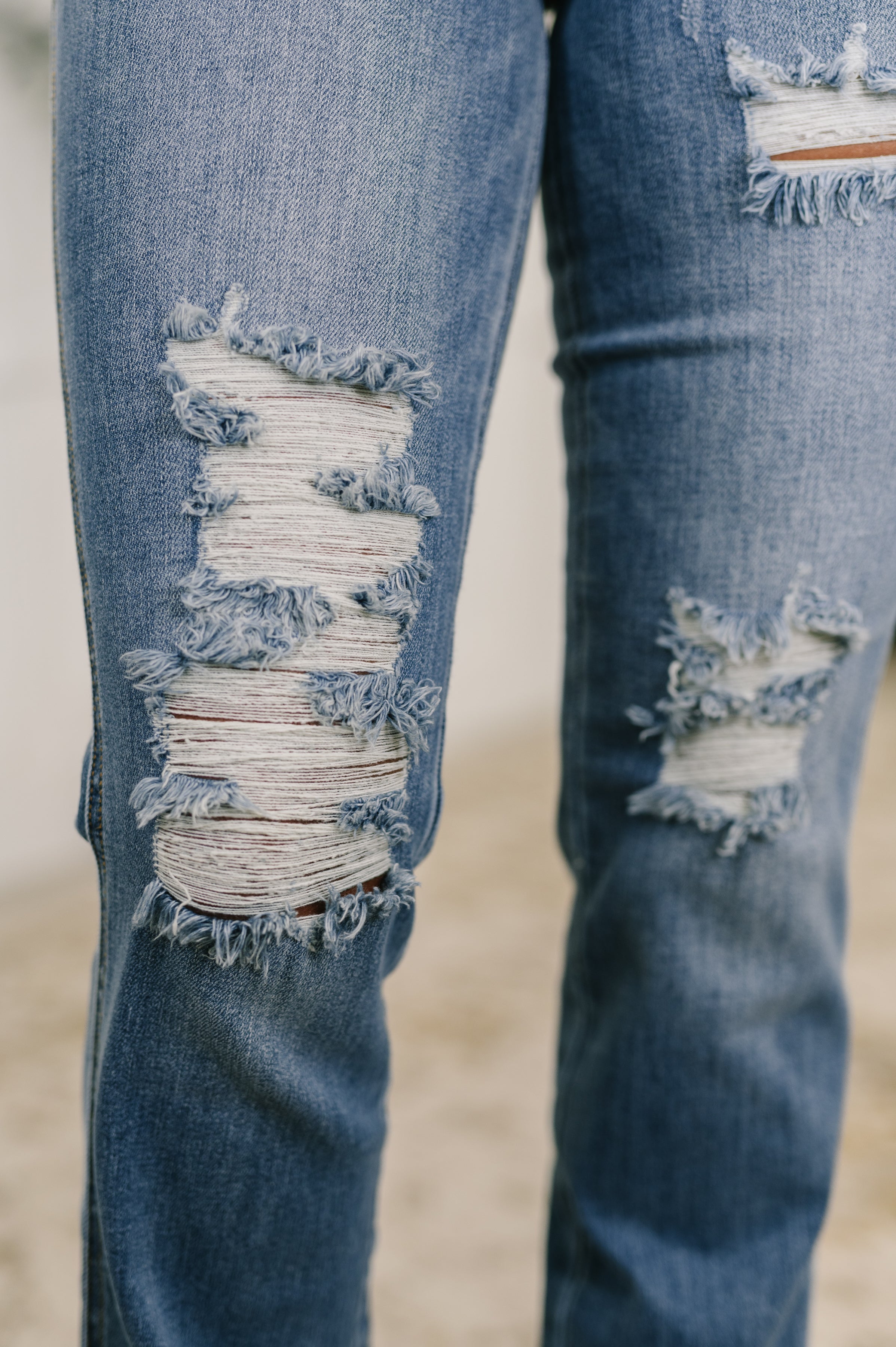 Close-up of blue distressed denim showing frayed high-rise bootcut jeans with large tear details on thighs
