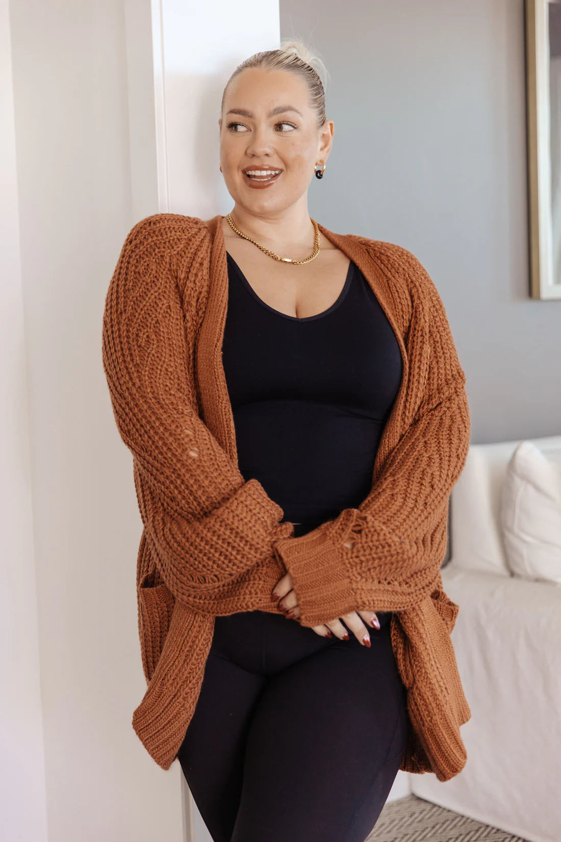 Woman wearing a chestnut knit cardigan with textured knit and large ribbed cuffs over a black top indoors