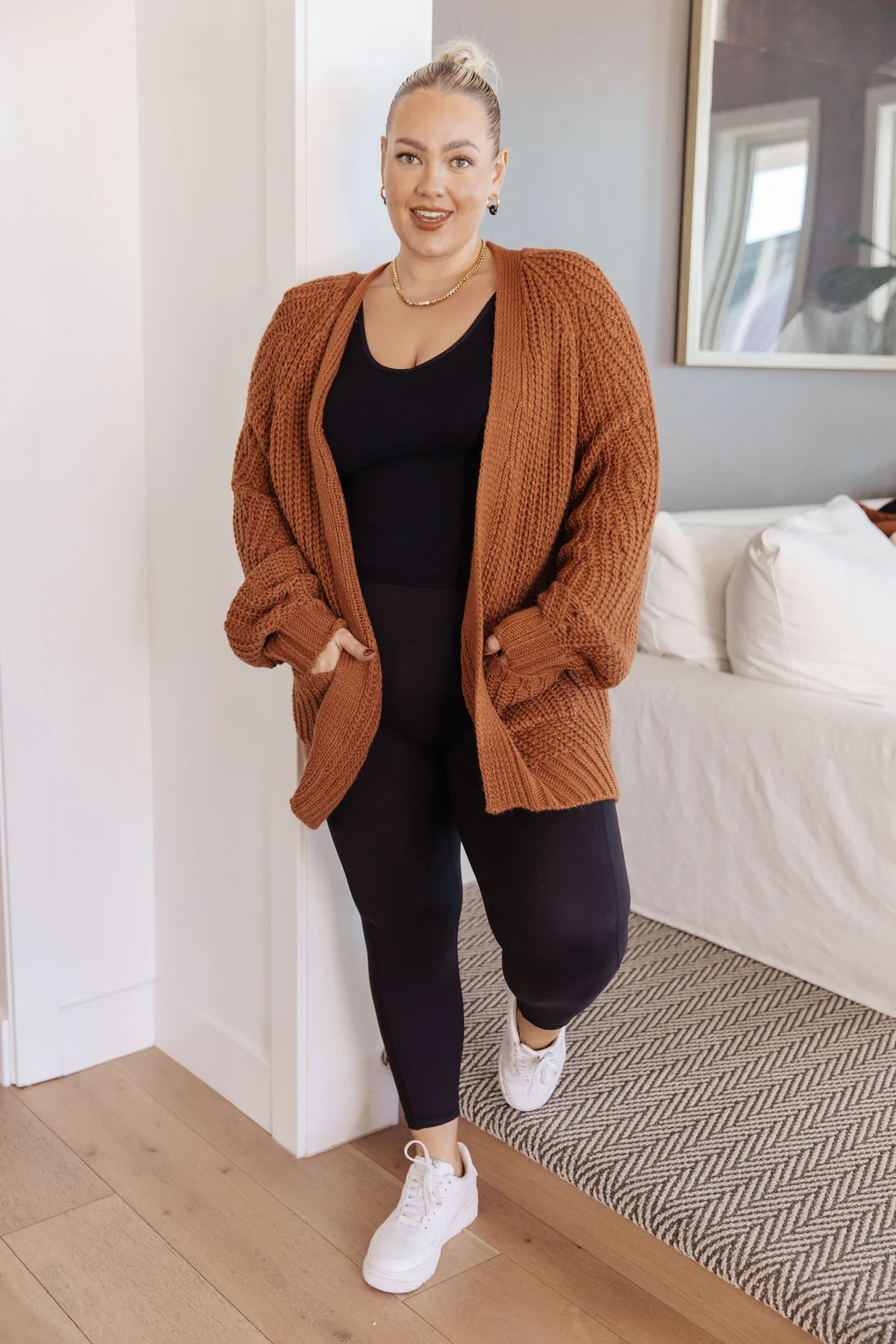 Plus-size woman wearing a chestnut oversized knit cardigan with large front pockets and textured pattern indoors
