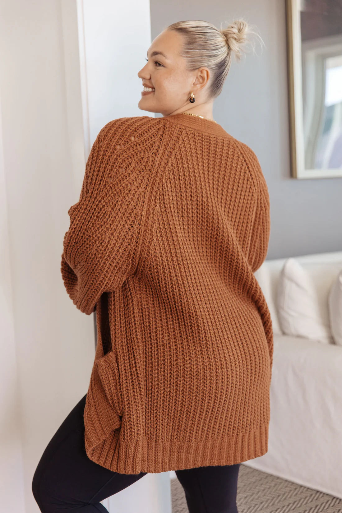 Woman smiling wearing a chestnut chunky knit cardigan with long sleeves and side pockets indoors