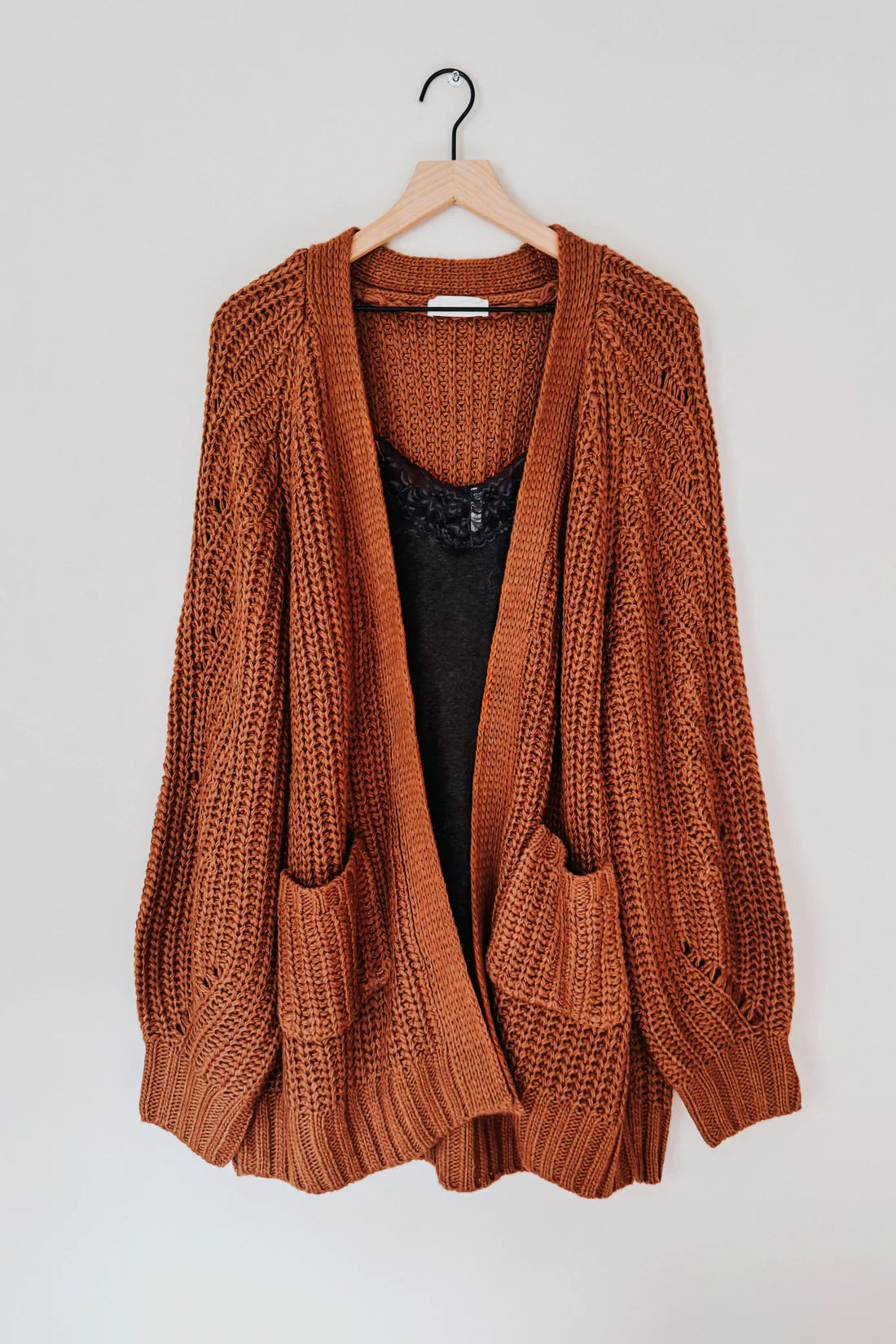 Chunky knit chestnut cardigan with oversized pockets and textured pattern layered over a black lace-trimmed top on hanger