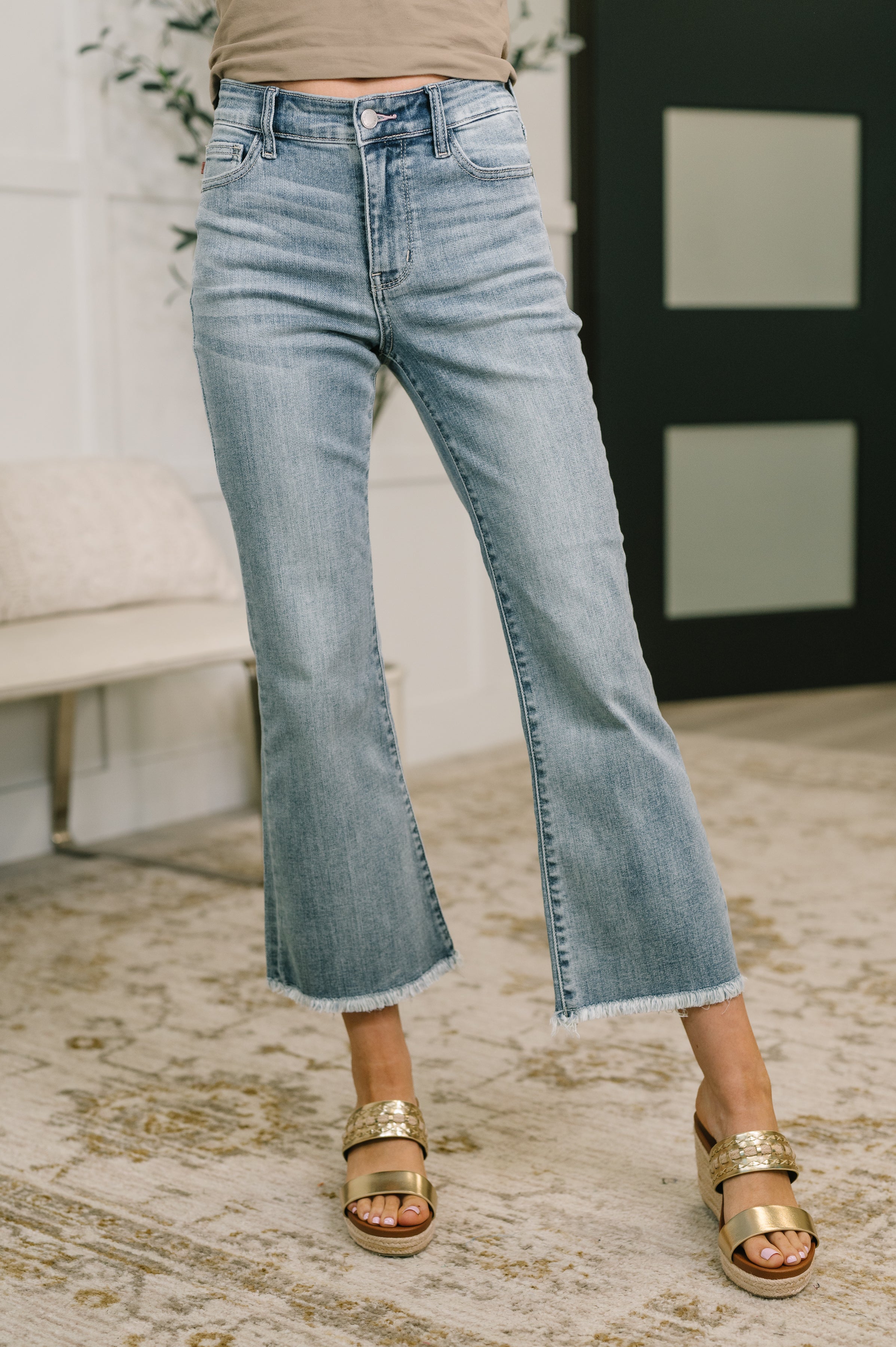 Woman wearing mid-rise blue kick flare jeans with frayed hem paired with gold strappy sandals indoors