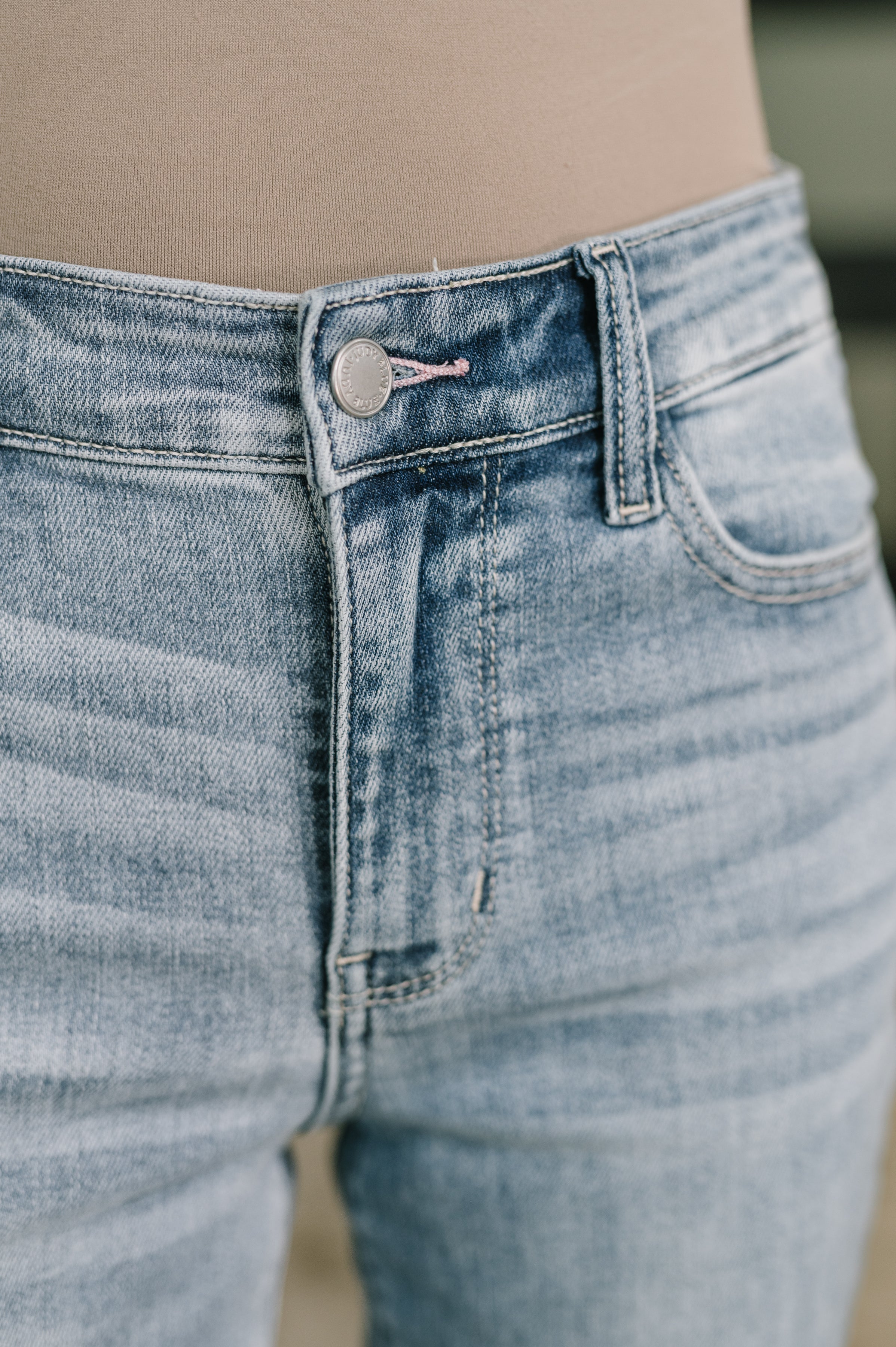 Close-up of light blue mid rise jeans with button detail and subtle whiskering on soft denim fabric