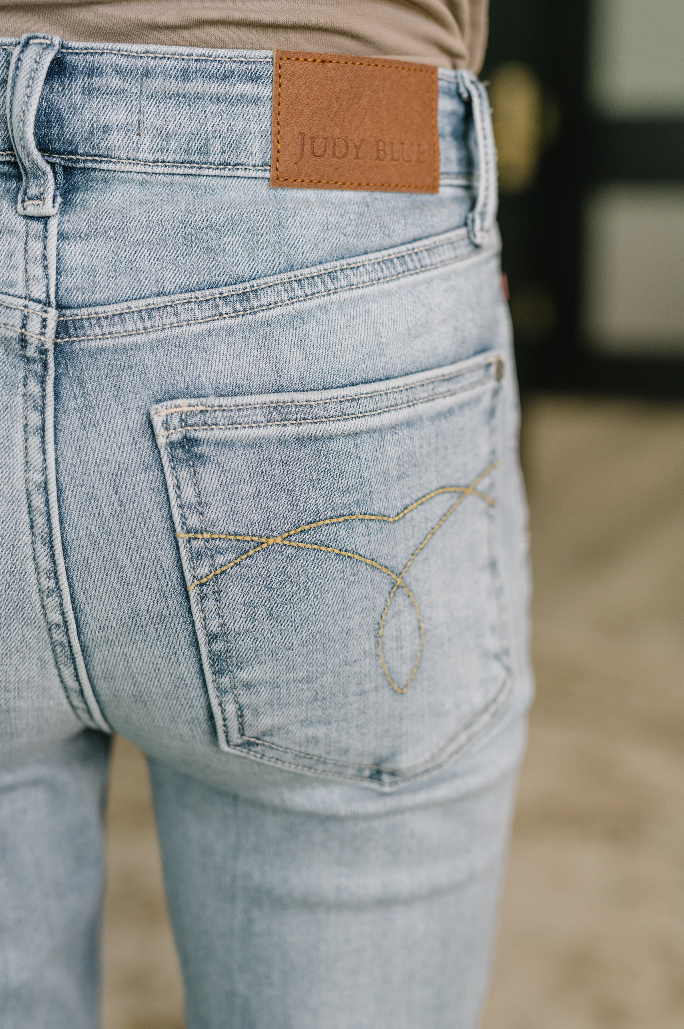 Close-up of light blue mid-rise jeans with stitched back pocket detail and brown leather patch above waistband