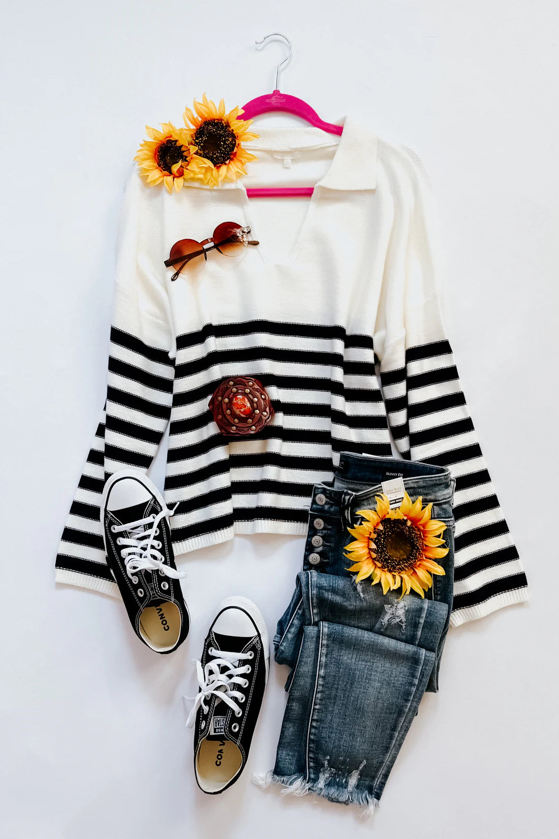 White sweater with black horizontal stripes and a collar, paired with distressed dark wash jeans, black sneakers, sunglasses, and decorative sunflowers.
