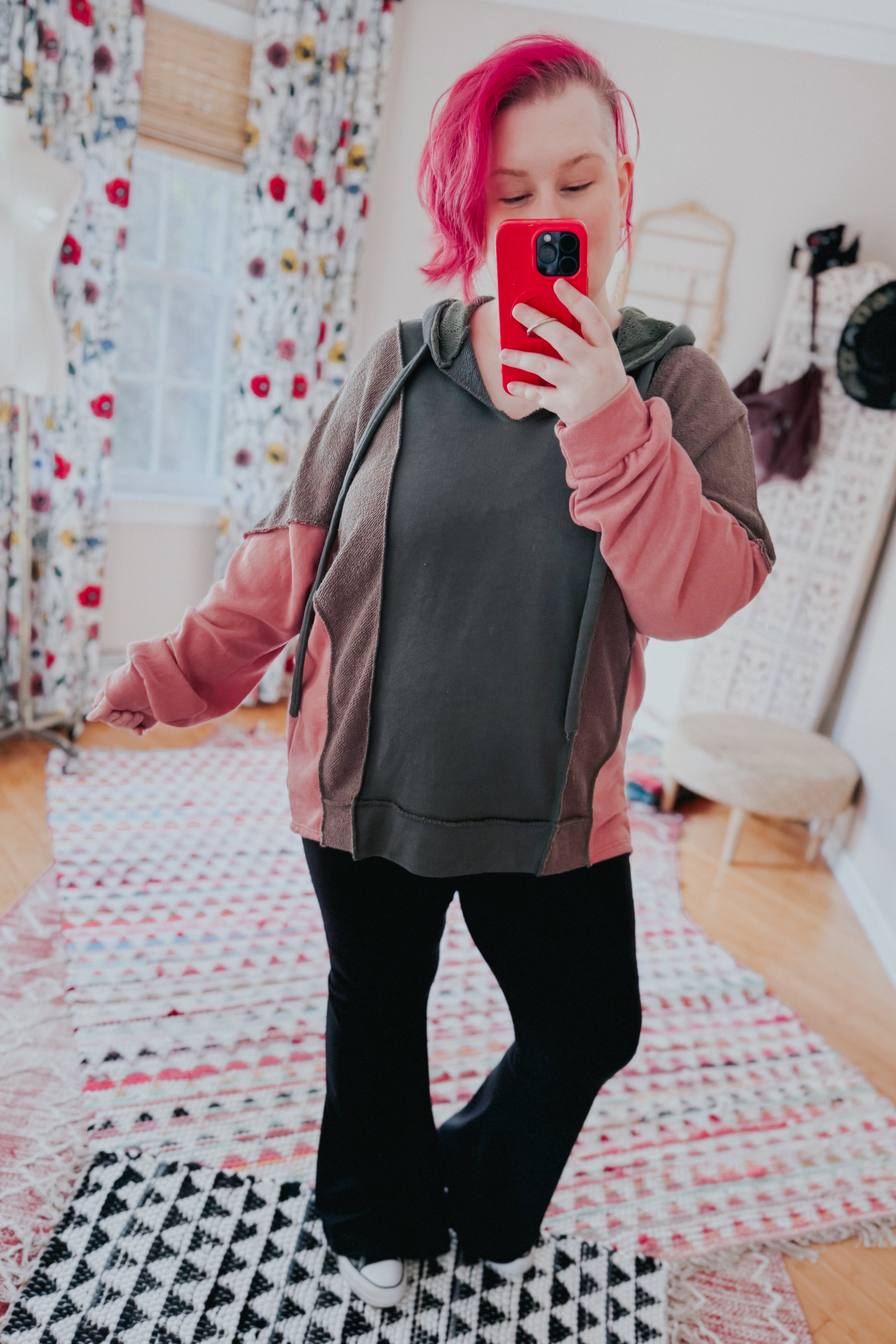 Woman with bright pink hair wearing a relaxed fit Message Me Back hoodie in sage, muted brown, and soft pink taking a mirror selfie indoors on patterned rugs.