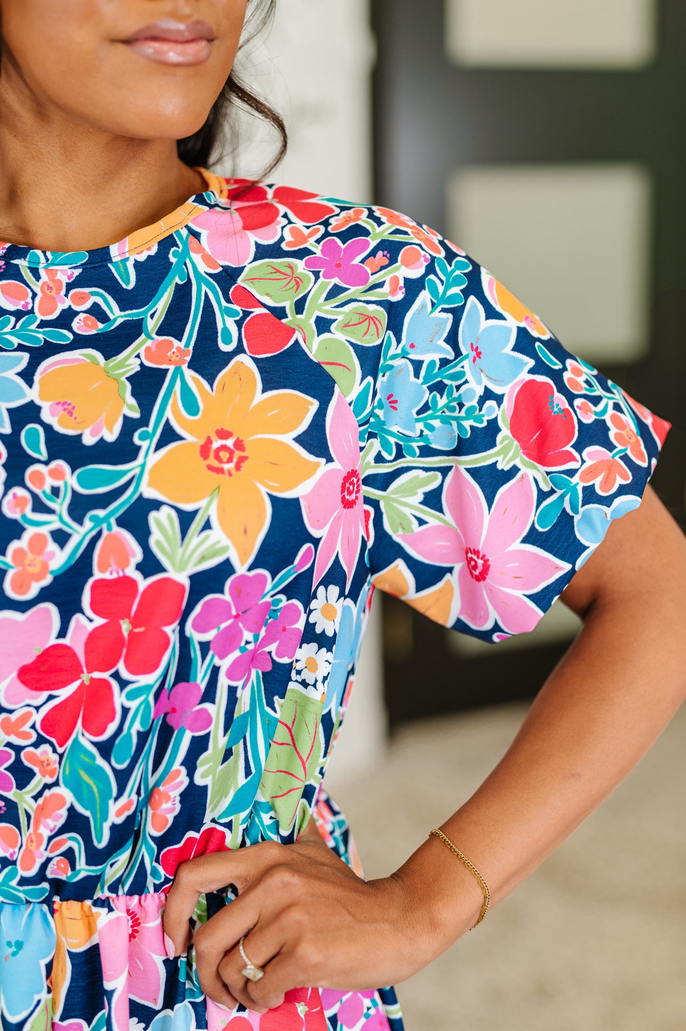 Close-up of woman wearing a navy dress with vibrant multicolored floral pattern and short puffed sleeves indoors