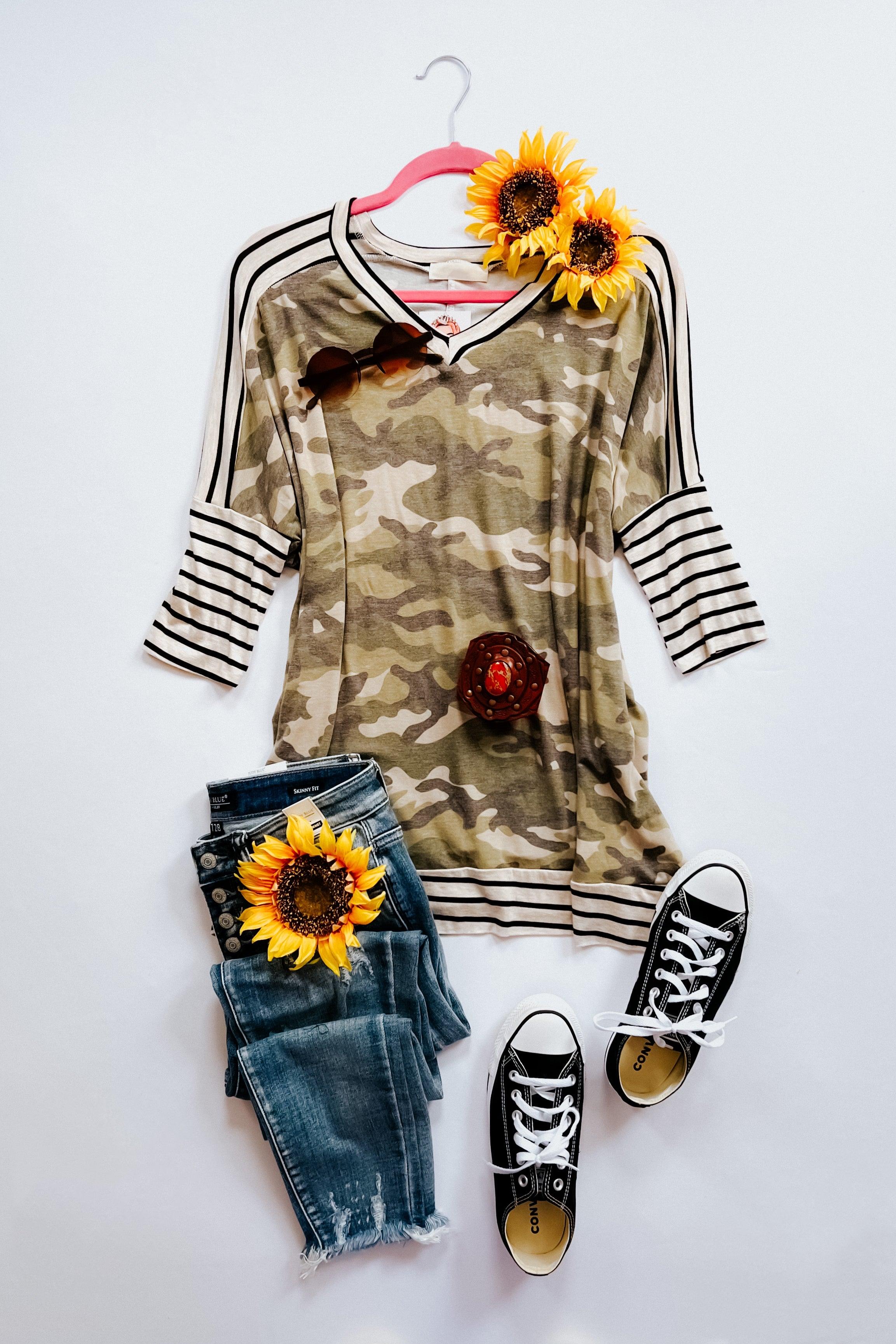 Green camo patterned mid sleeve tunic with black and white striped cuffs and trim, styled with blue jeans, black sneakers, and sunflowers.