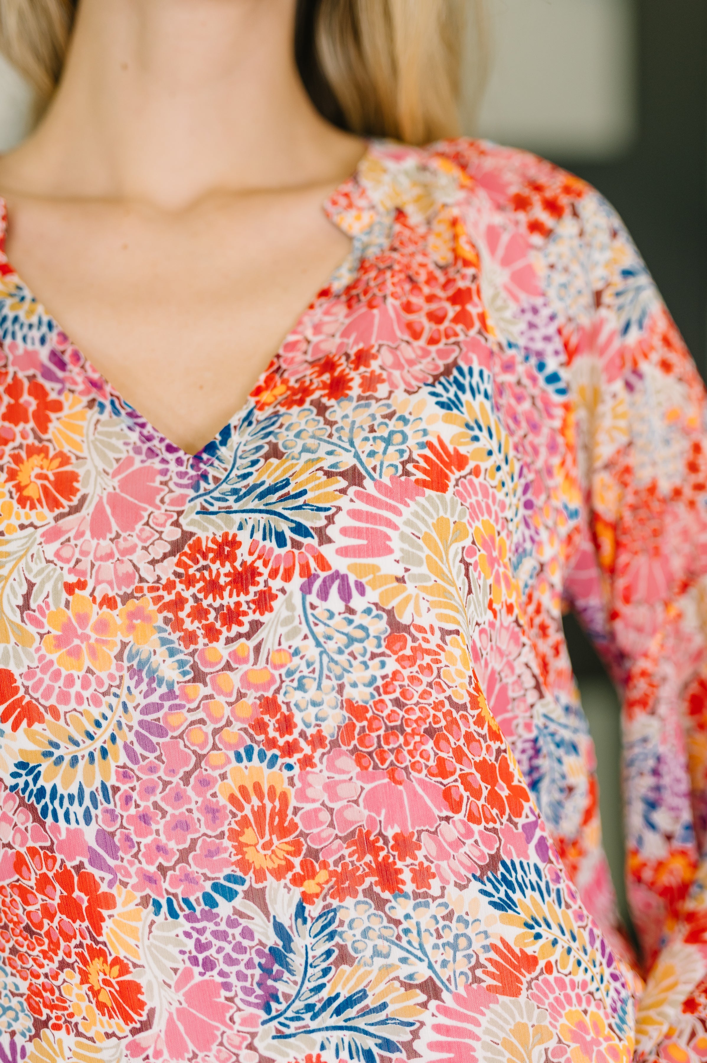 Close-up of woman wearing a vibrant red floral top with a v-neckline and colorful botanical print