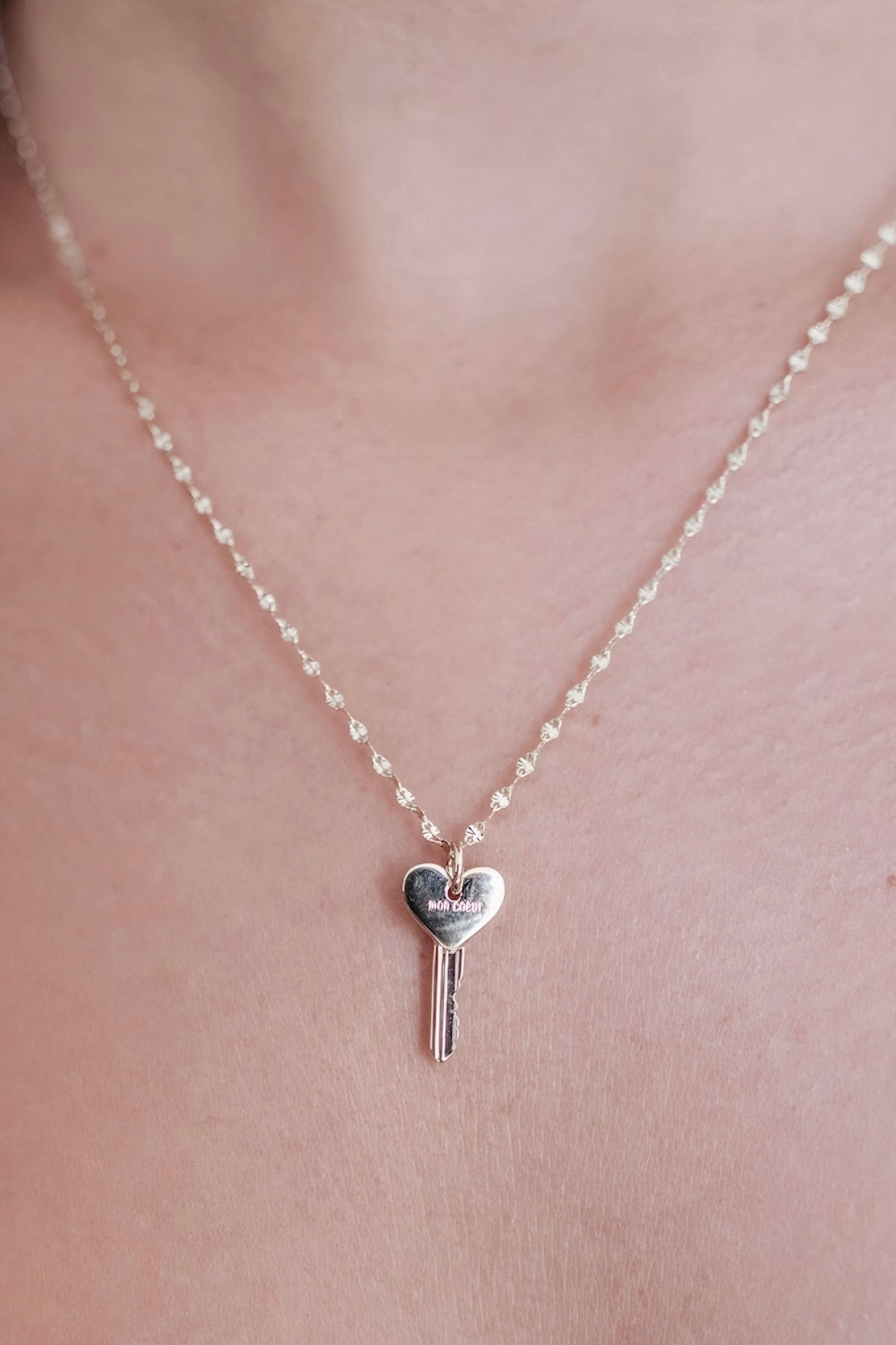 Delicate gold necklace with a heart-shaped key pendant engraved with subtle lettering, resting gently against the skin.