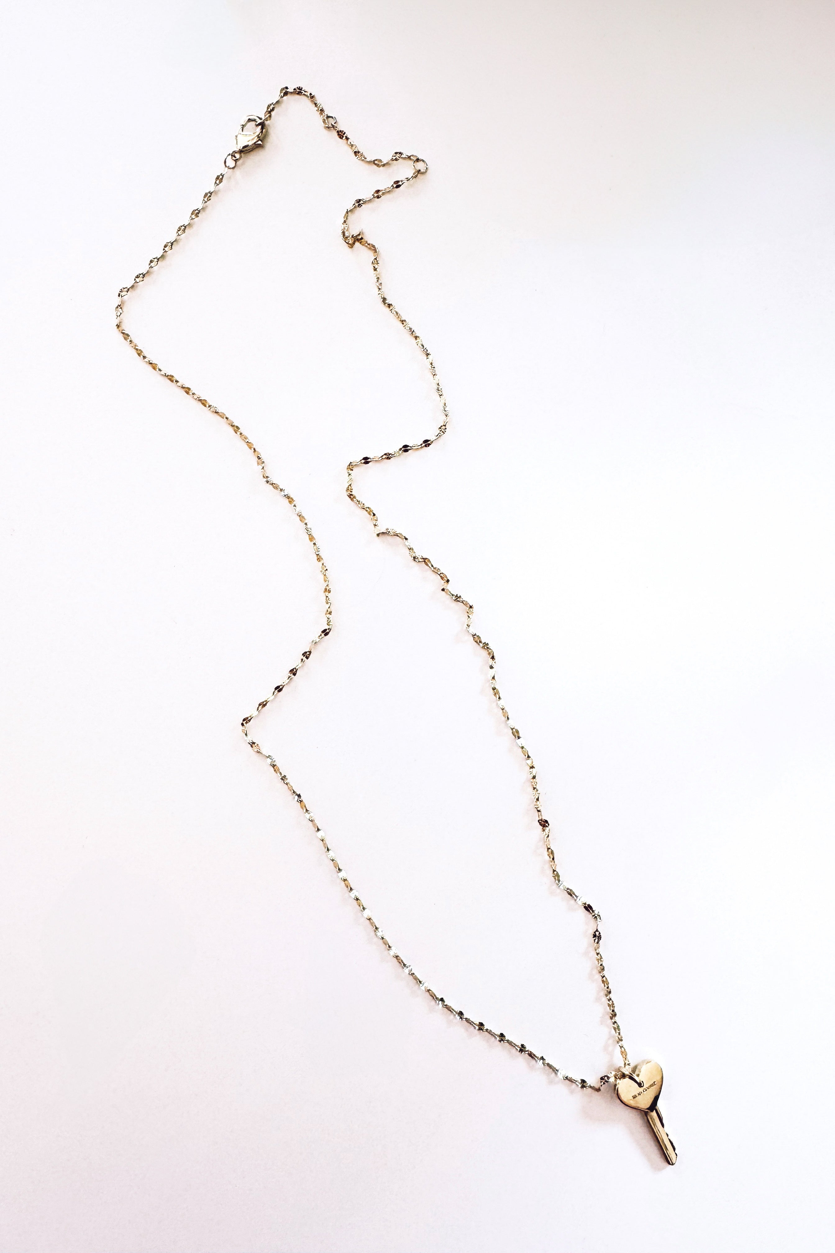 Delicate gold chain necklace featuring a small key pendant with a heart-shaped top, displayed against a clean white background.