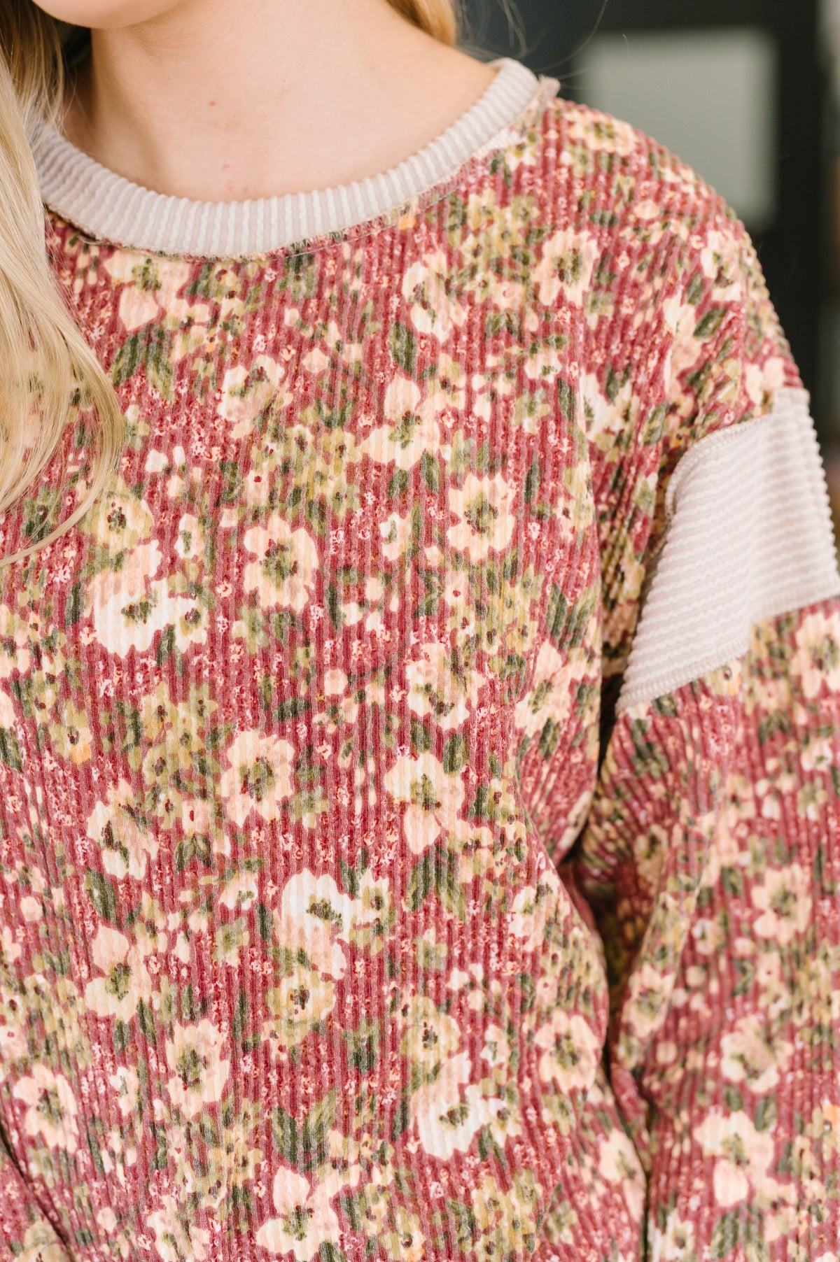 Close view of a woman wearing a rust floral textured knit top with a ribbed round neckline and cream sleeve stripe